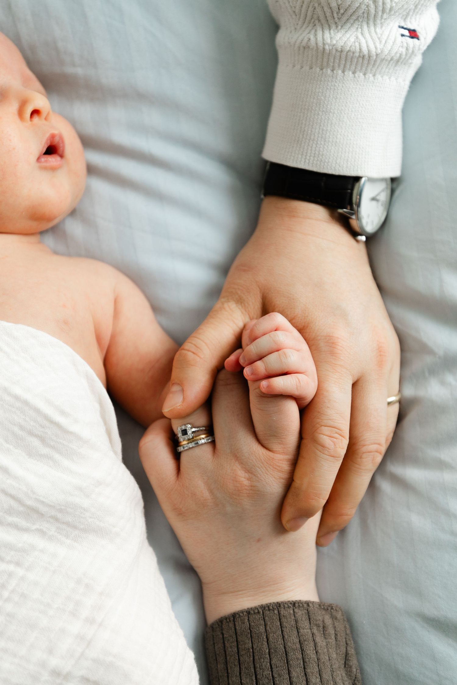 Close-up of parent and baby holding hands with wedding ring visible.