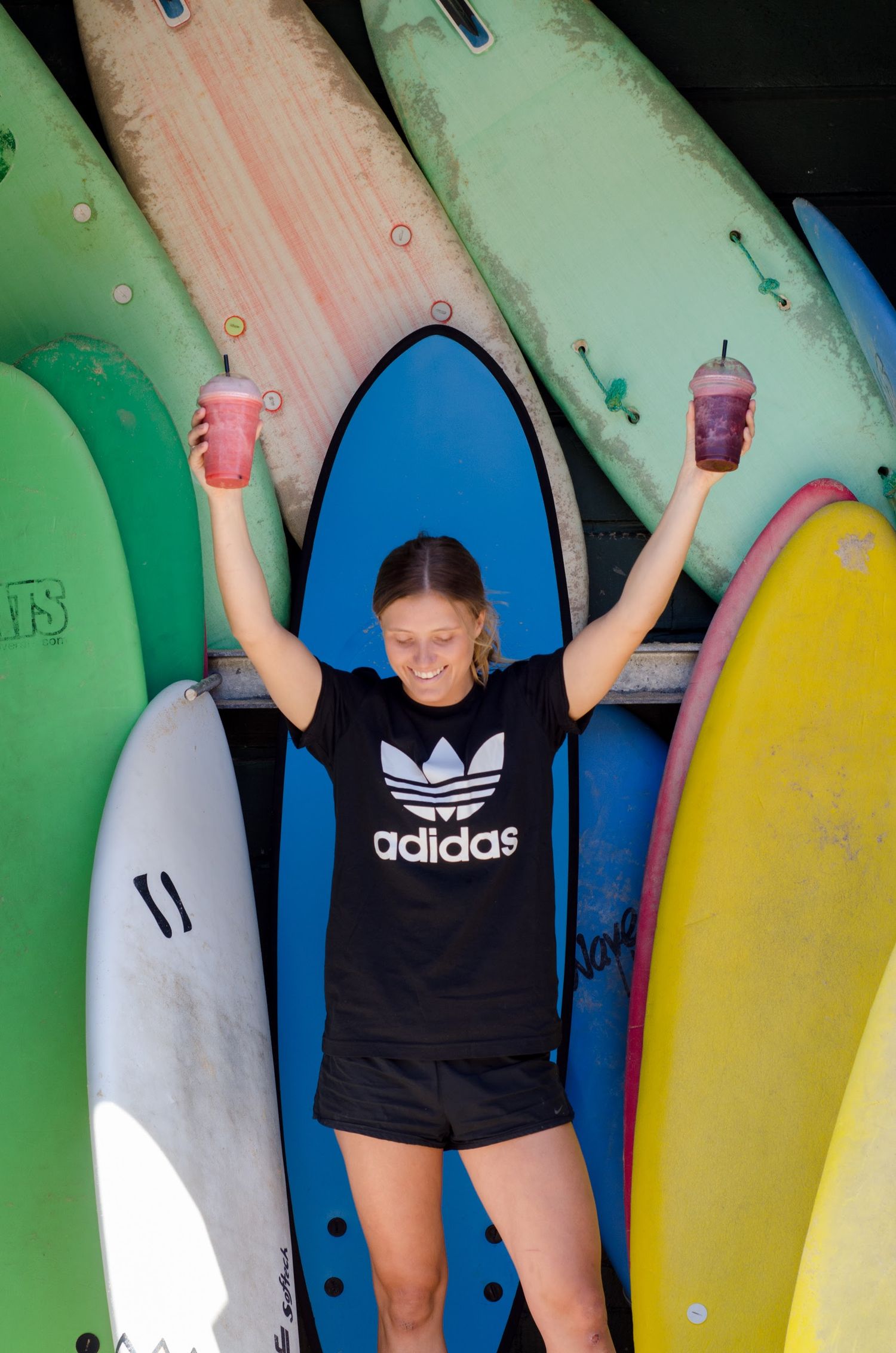 A person poses playfully in front of colorful surfboards lined up against a wall.