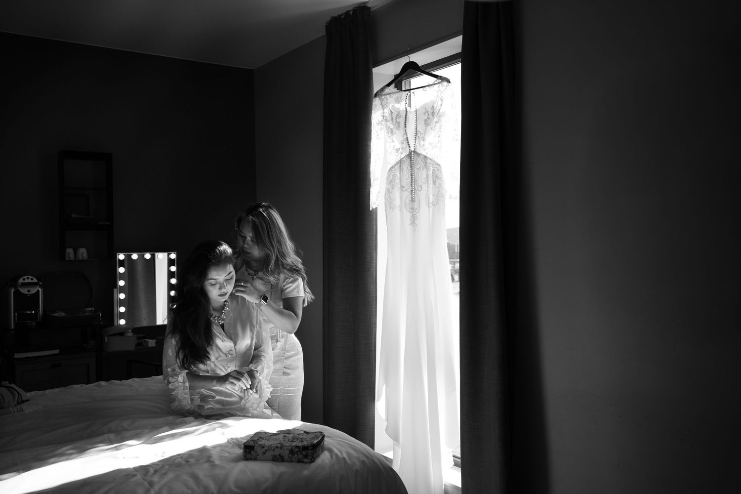 Dramatic silhouette of a wedding dress hanging in a sunlit window.