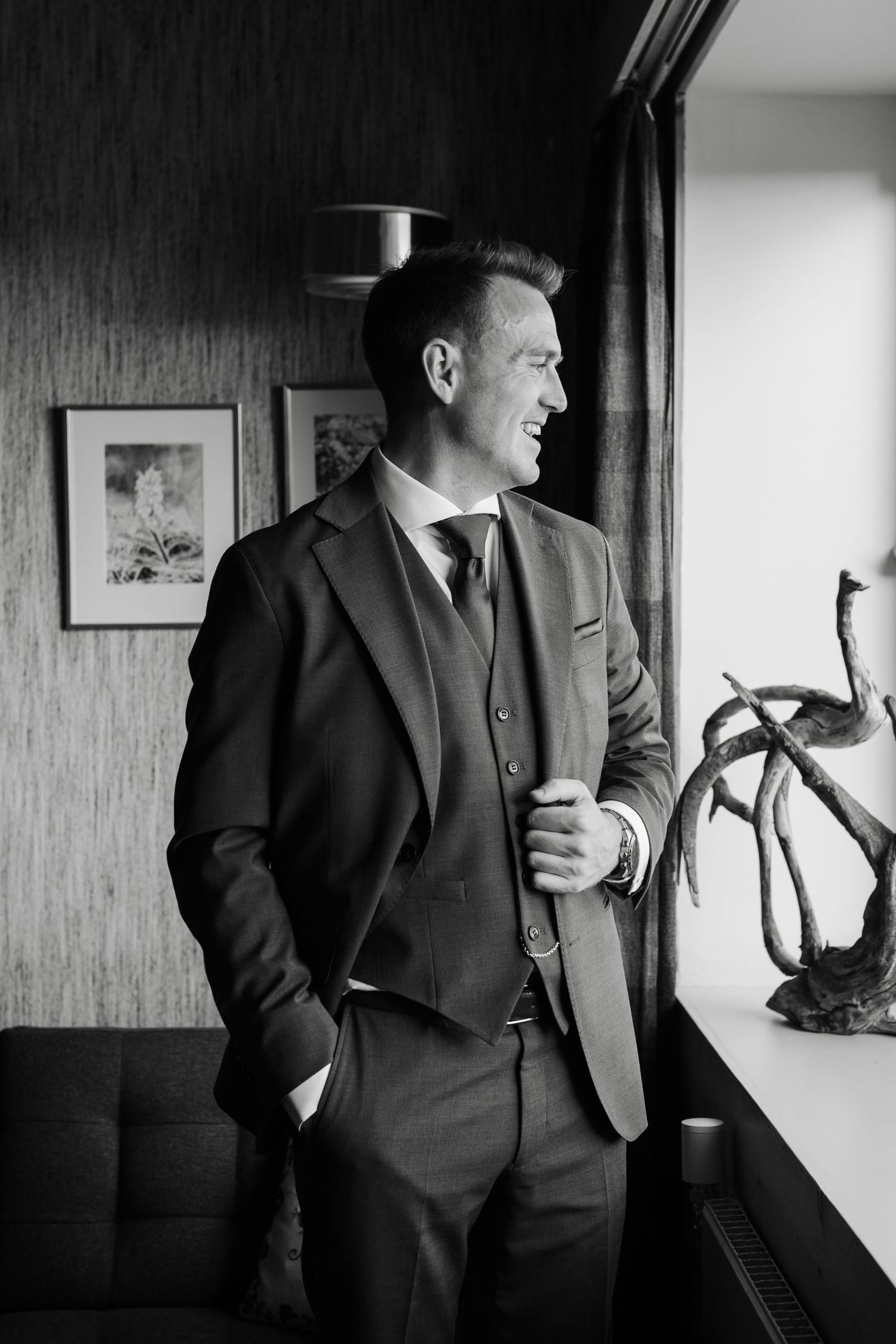 Black and white photos showing a suited man standing by windows in an interior space.