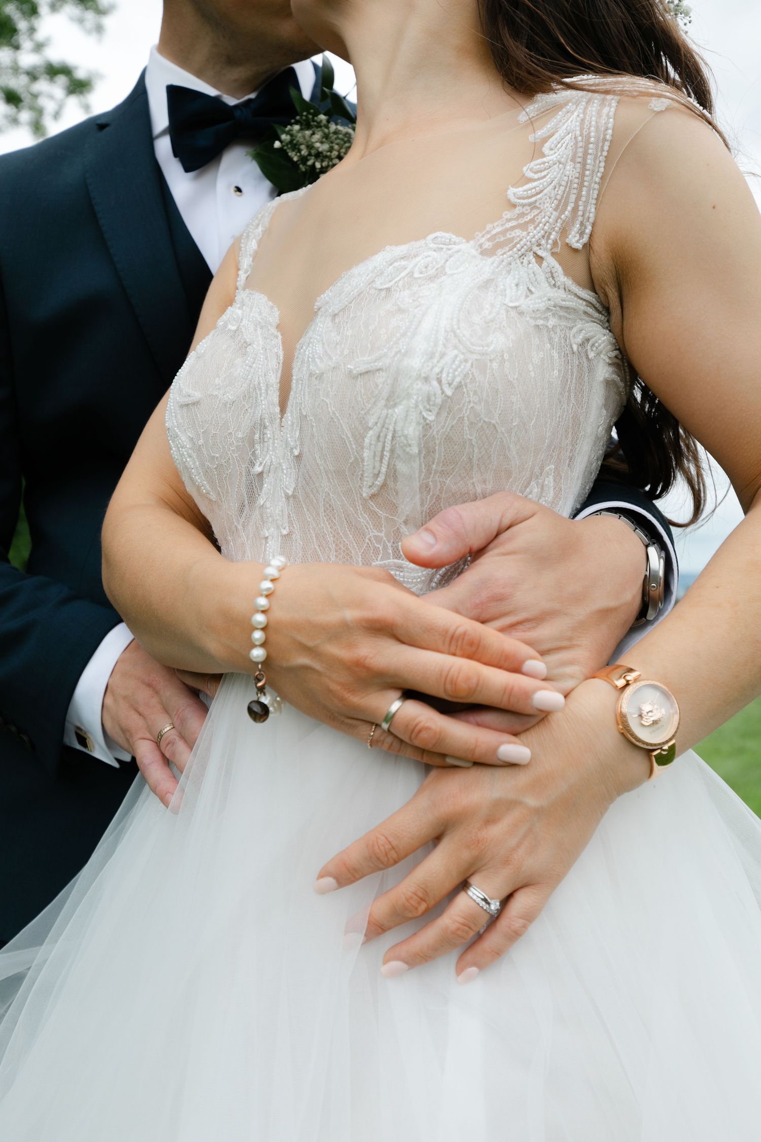 Close-up of hands showing wedding rings and lace details on a white wedding dress.