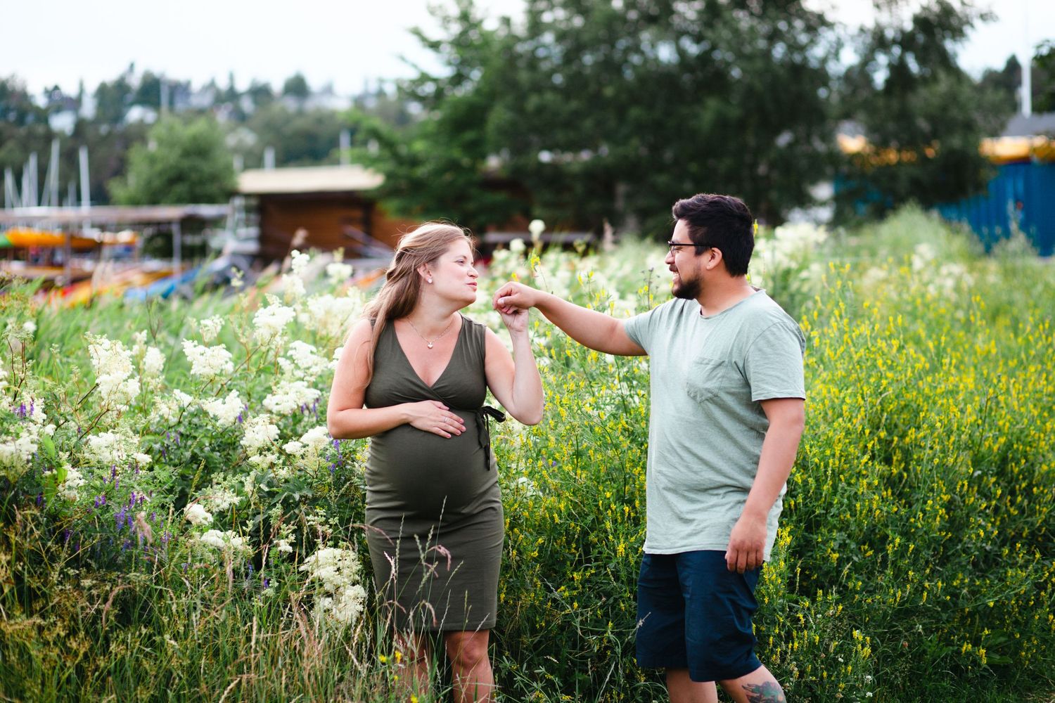 Couple sharing intimate moments during outdoor maternity photoshoot among yellow wildflowers.