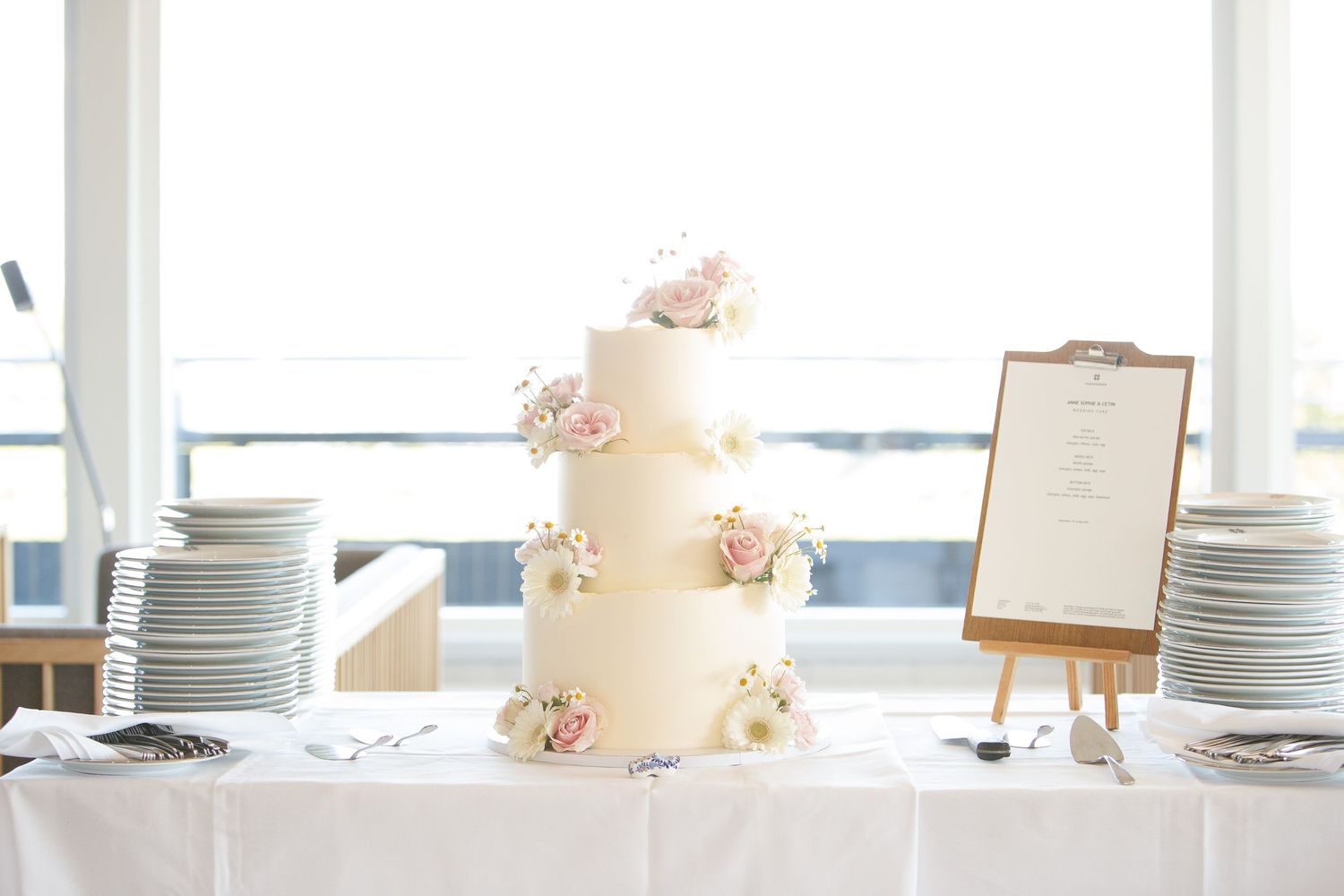 Elegant white wedding cake and place settings displayed on reception table.