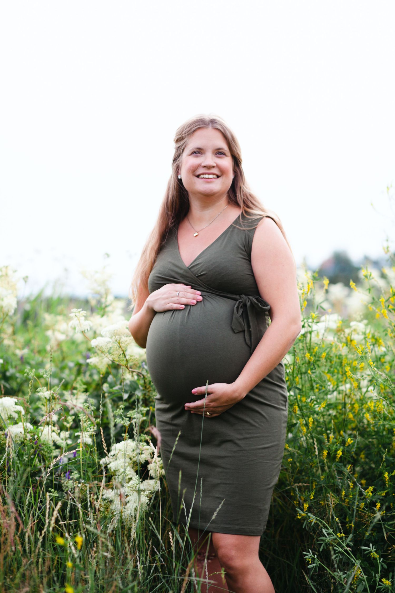 Maternity photo session in a wildflower meadow with green dress and natural lighting.