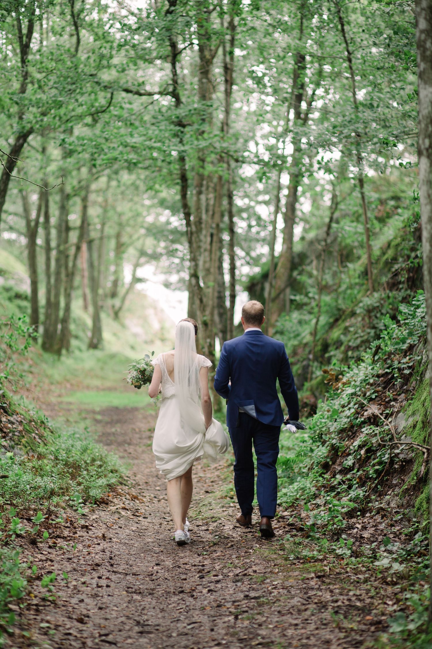 Couple walking hand in hand down a wooded forest path after their wedding ceremony.