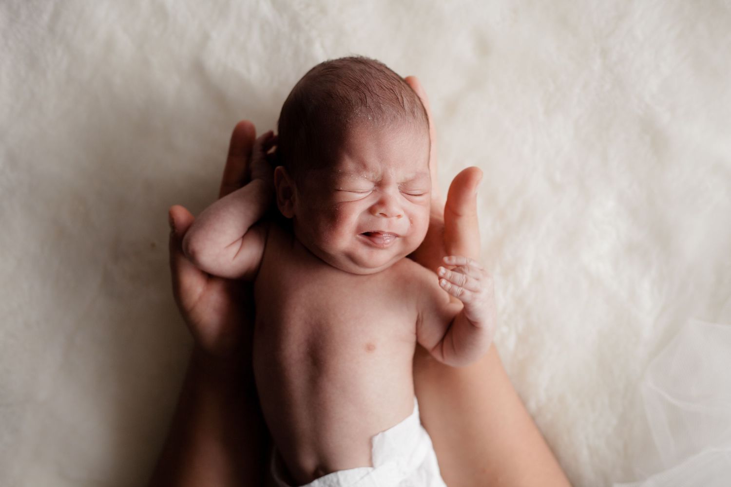 Gentle hands cradling a sleeping newborn baby on soft white fabric.