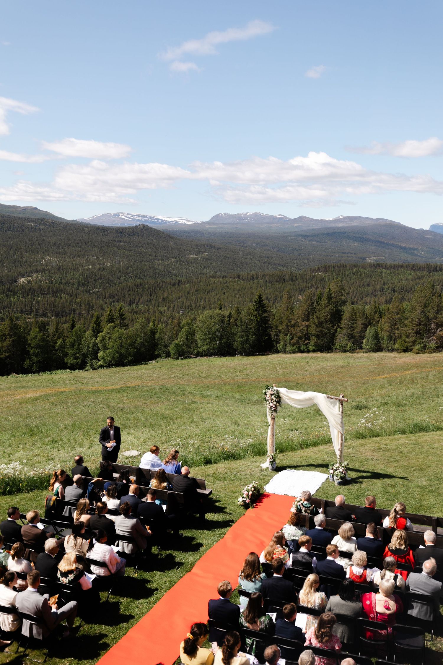 An outdoor mountain wedding ceremony setup with red carpet aisle and white chairs.
