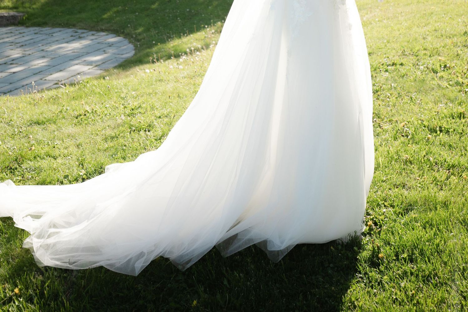 A flowing white wedding dress train trails elegantly across lush green grass in a garden setting.