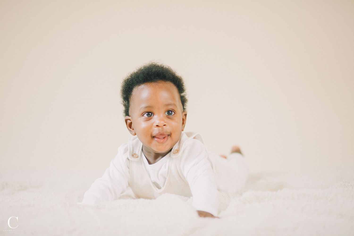 Baby in white outfit smiling on light neutral background.