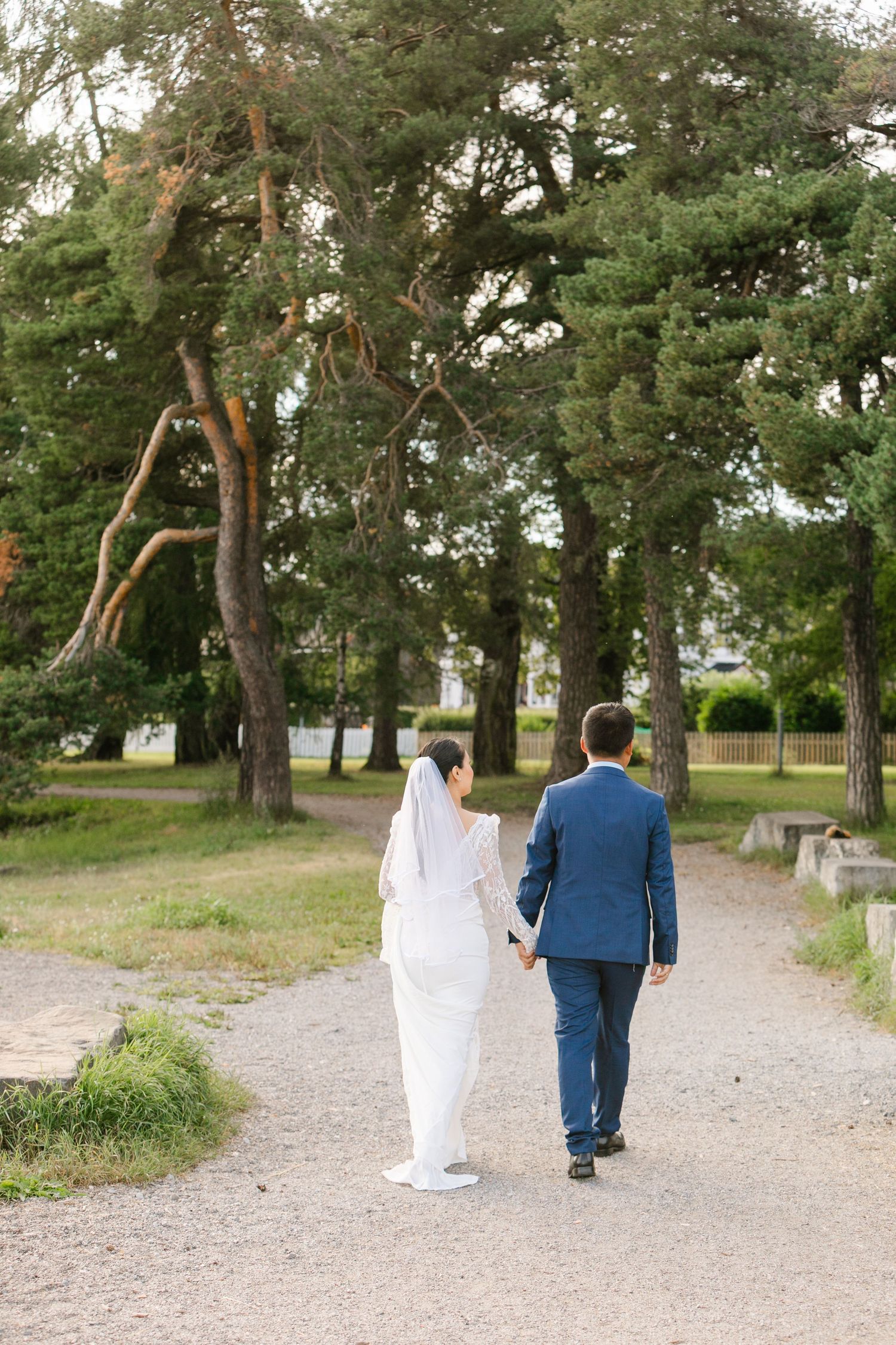 Newlywed couple walking down a tree-lined path in wedding attire.