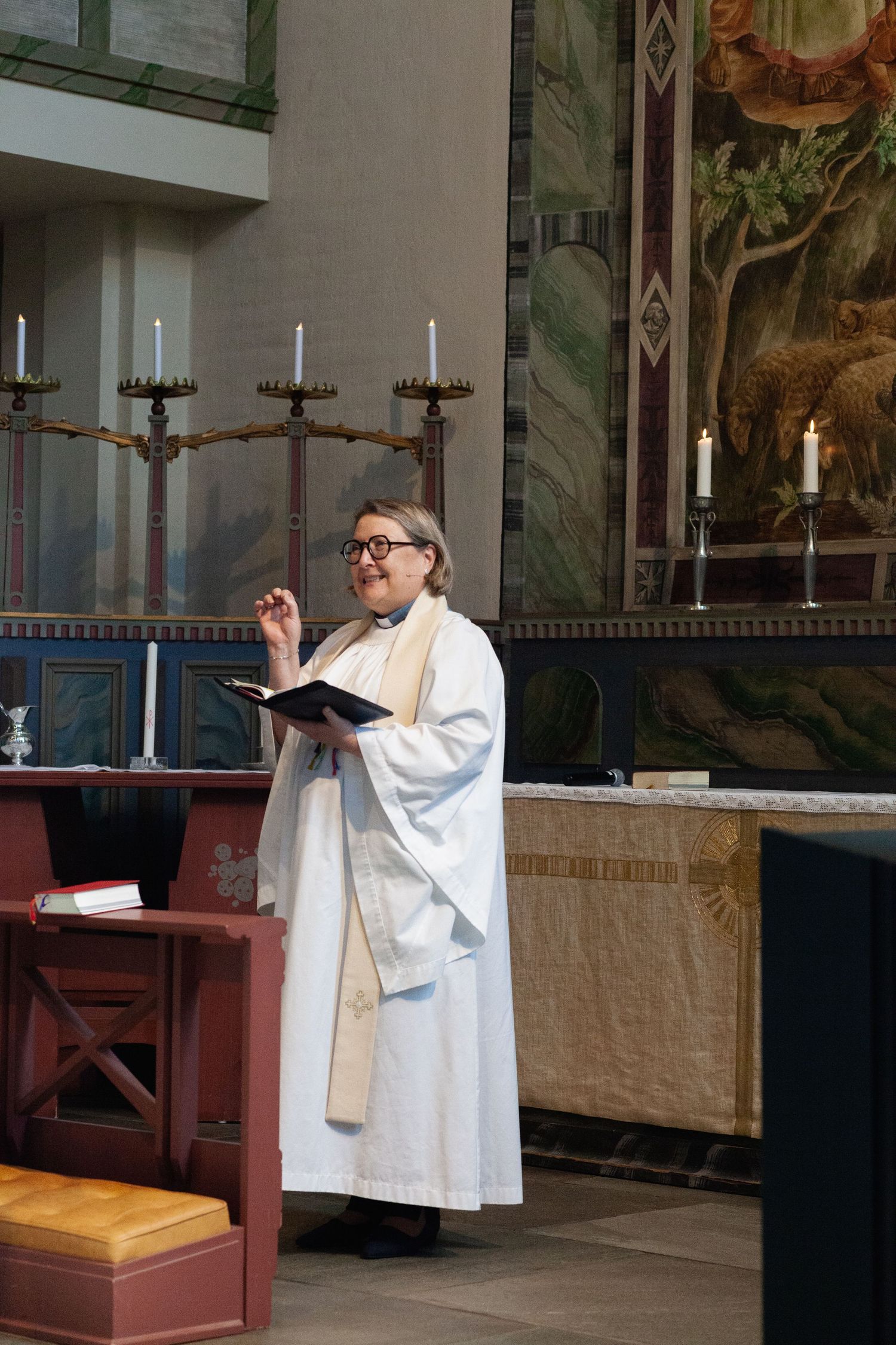 A church minister in white robes conducts a religious ceremony at the altar.