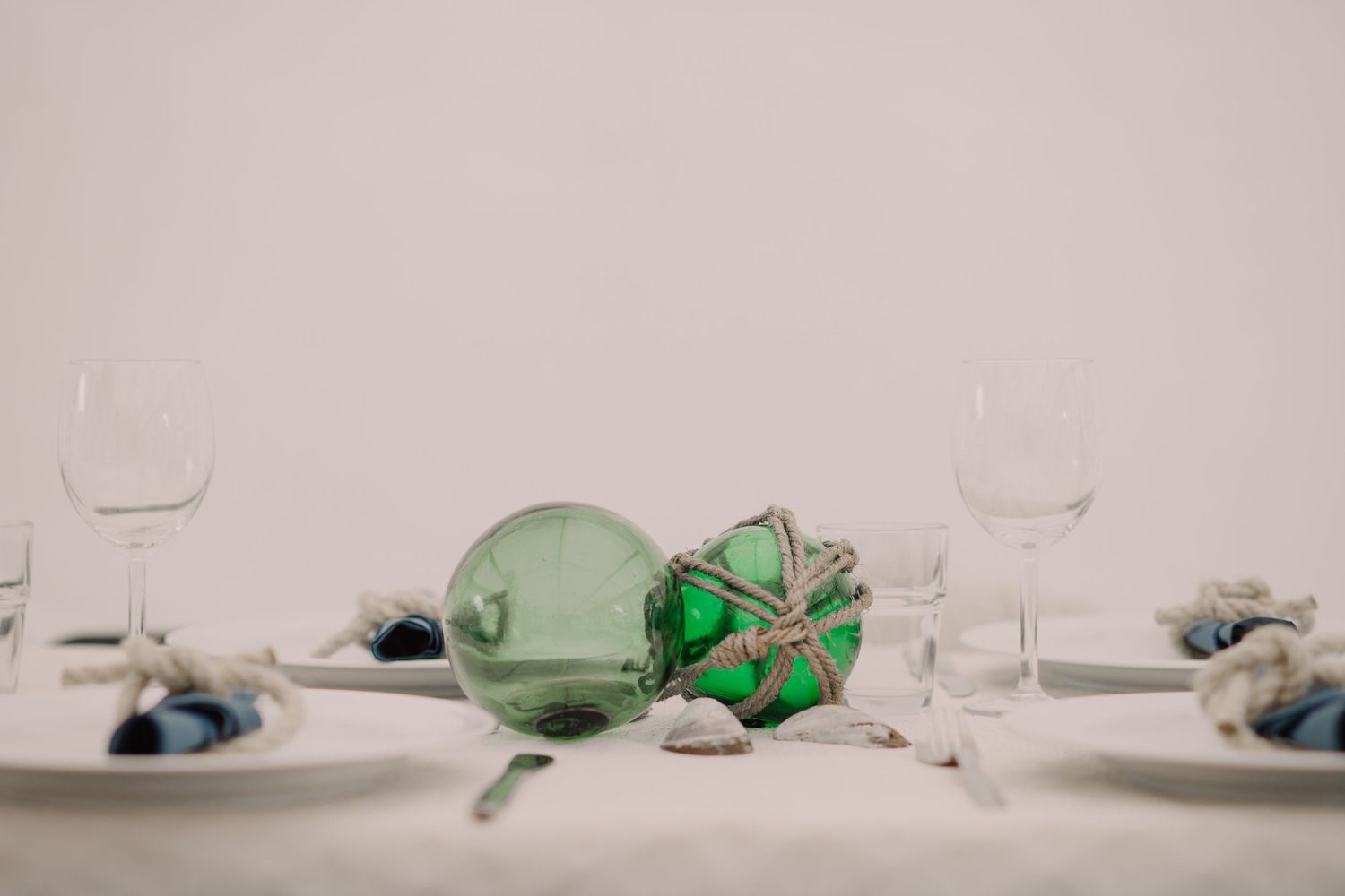 Minimalist table setting with white plates and green glassware.
