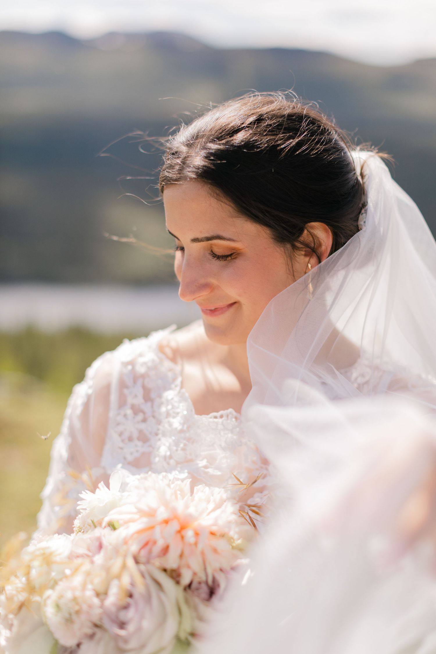 Close up of a bride with veil and bouquet against a mountain landscape.