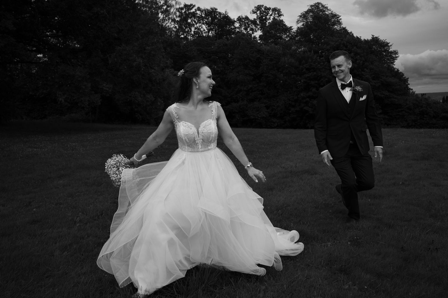 Wedding couple poses dramatically in black and white on grassy field.