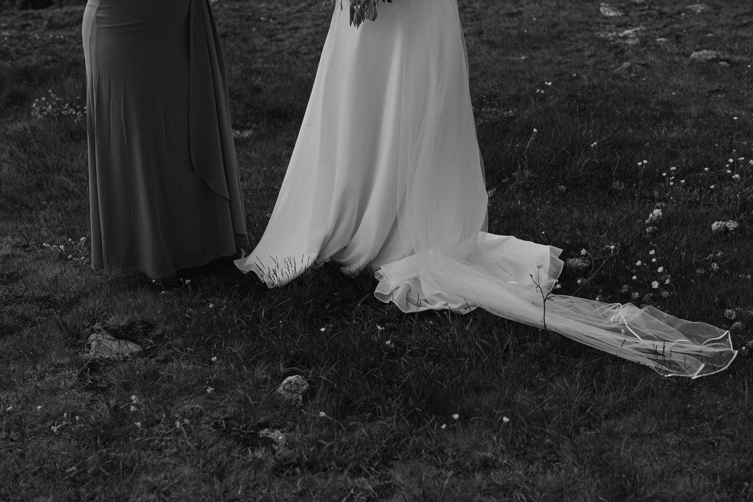 A black and white wedding photo captures a couple walking through nature.