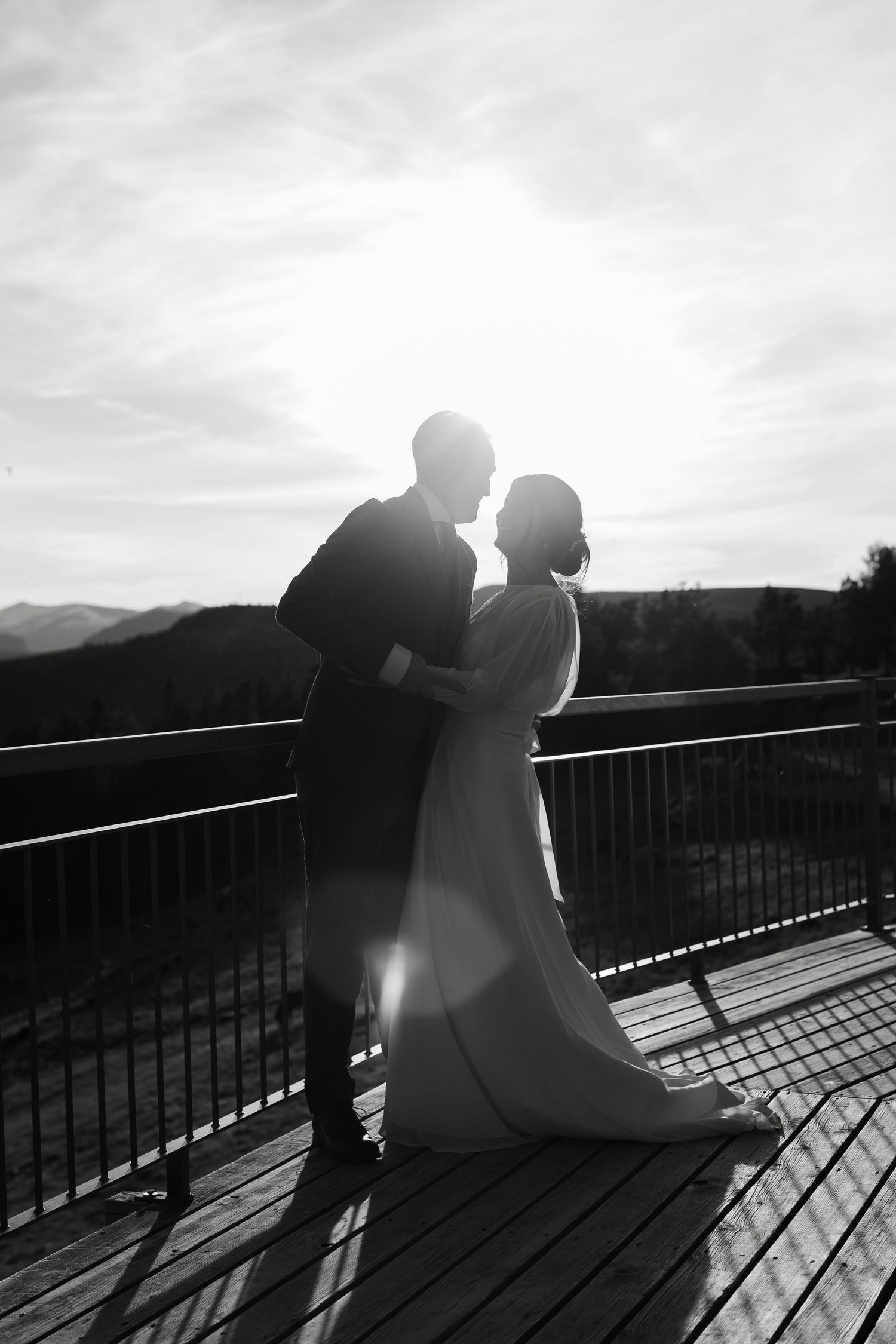Silhouetted couple on deck against dramatic mountain landscape at sunset.