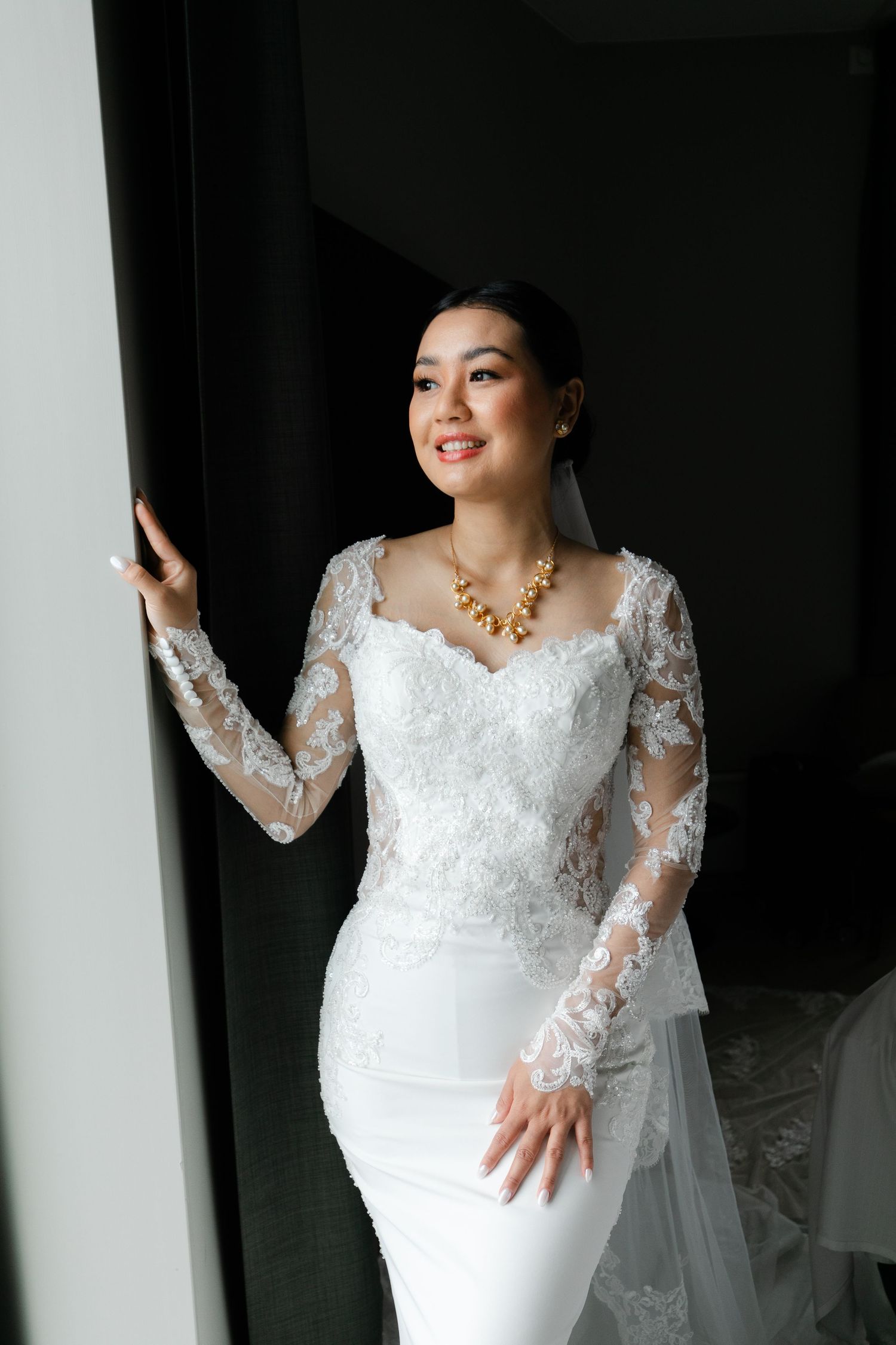 Elegant lace wedding dress details captured in dramatic window lighting.