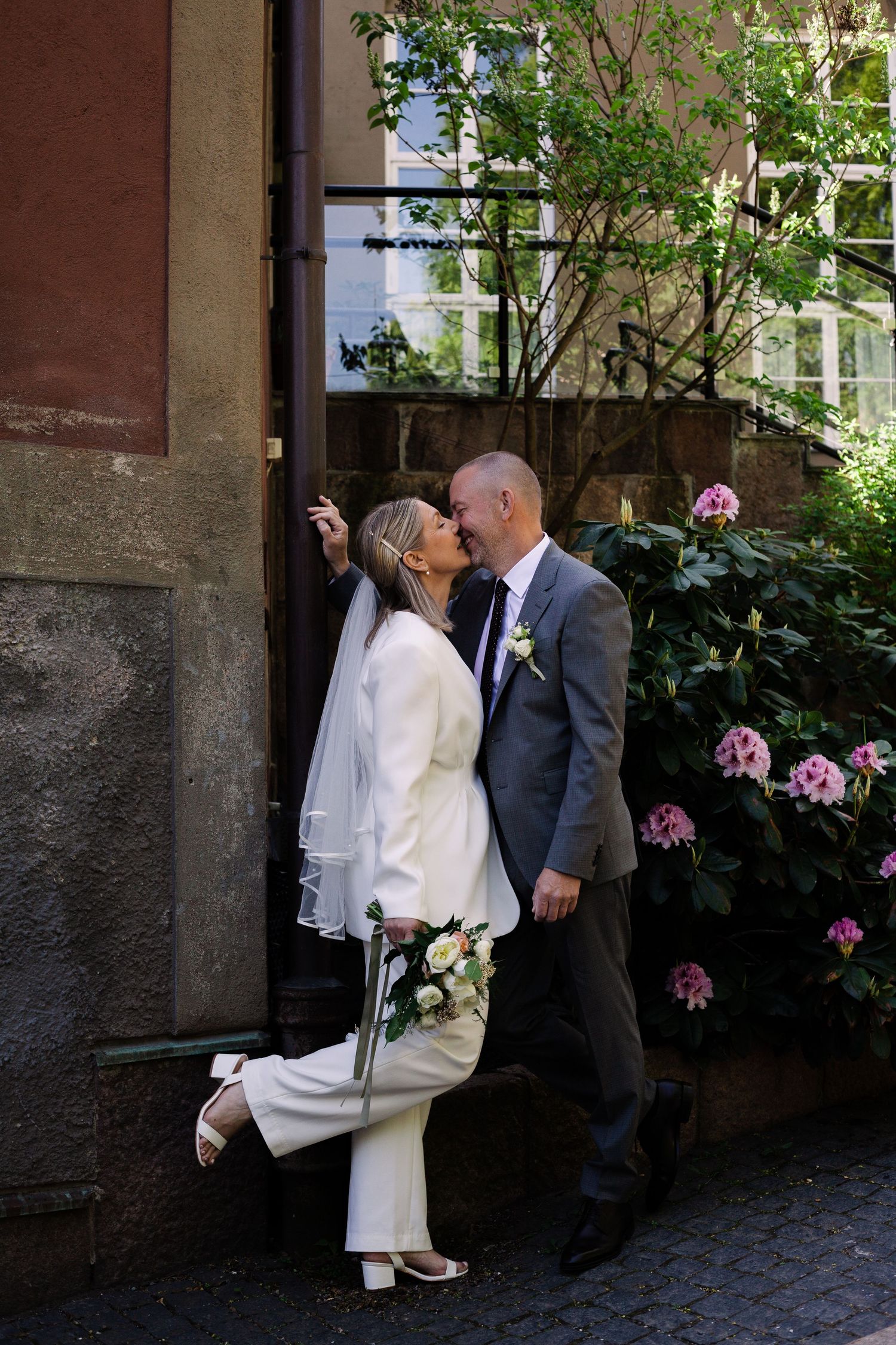 A romantic wedding moment captured in a garden setting with pink flowers blooming in the background.