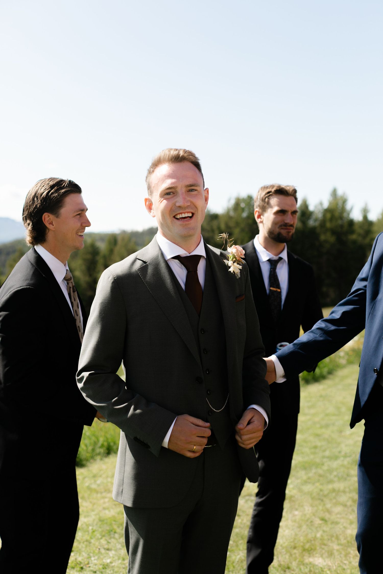 Group of groomsmen laughing together outdoors during wedding celebration.