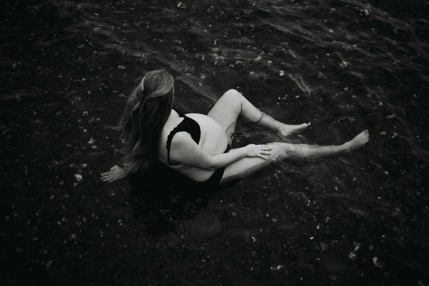 Dramatic underwater maternity photography with floating fabric in dark water.