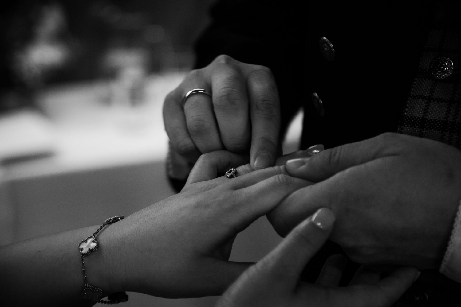 Close-up shot of hands exchanging rings during a ceremony in black and white.