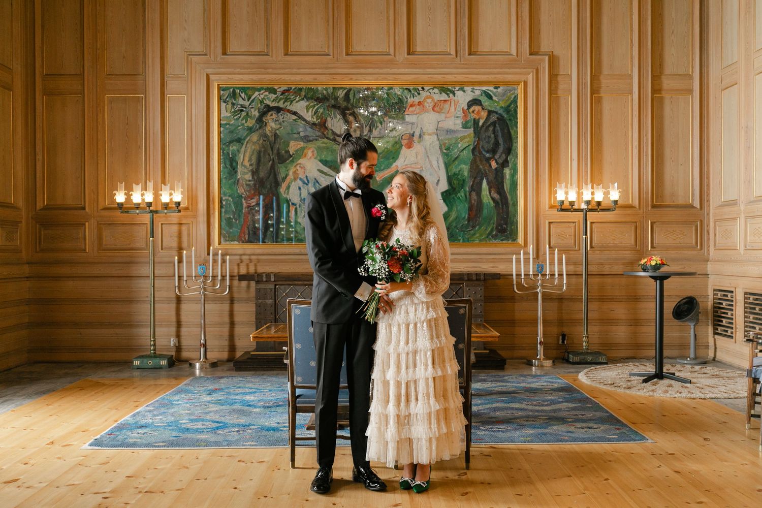Couple poses in formal attire against ornate wall with candelabras.
