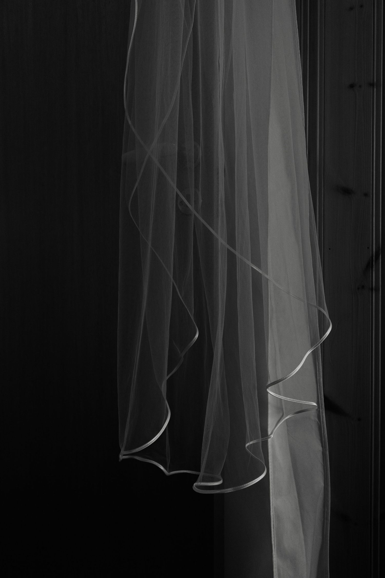 Flowing white wedding veil fabric photographed against a dark background.