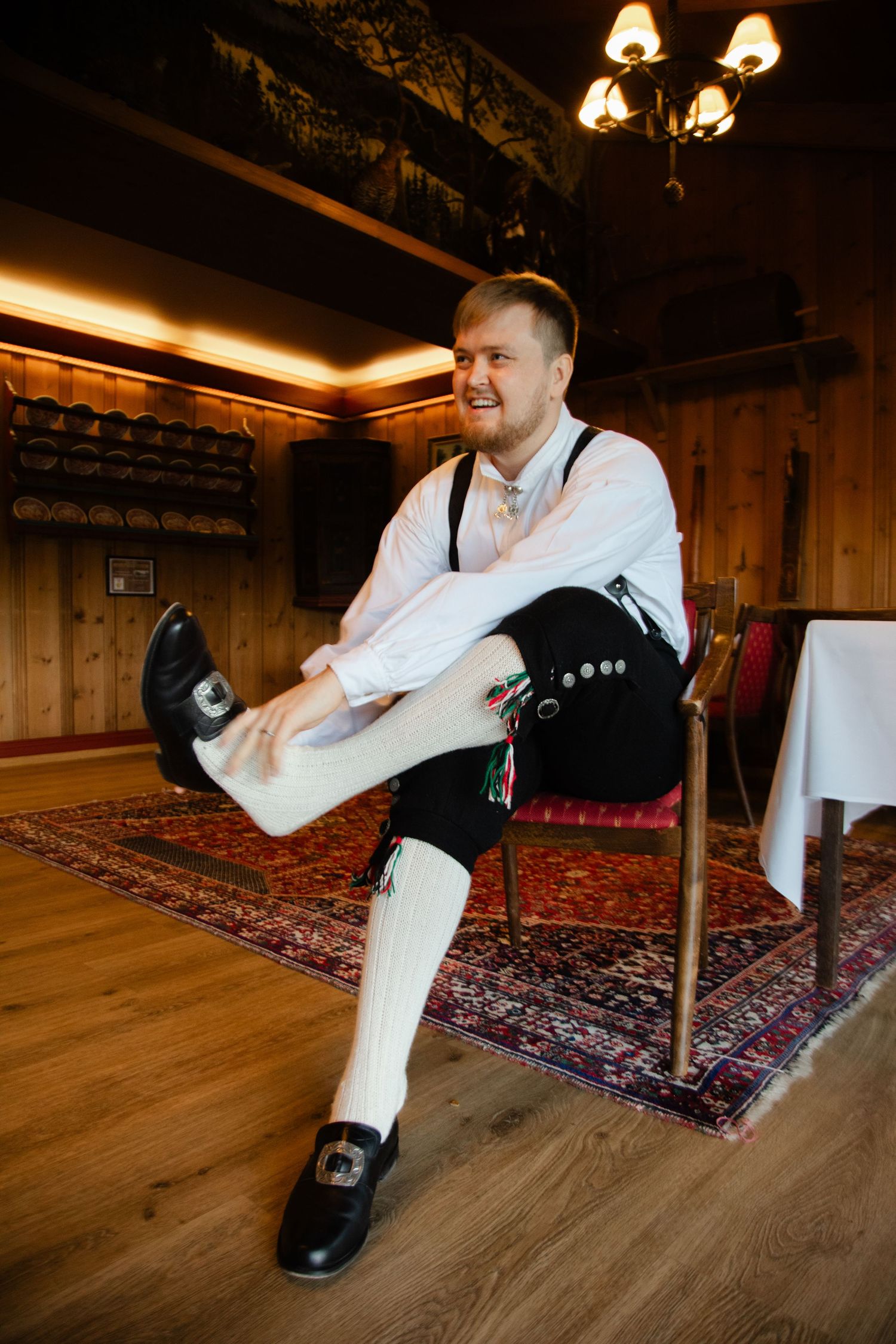 Wedding shoes and traditional attire details on a wooden floor with oriental rug.