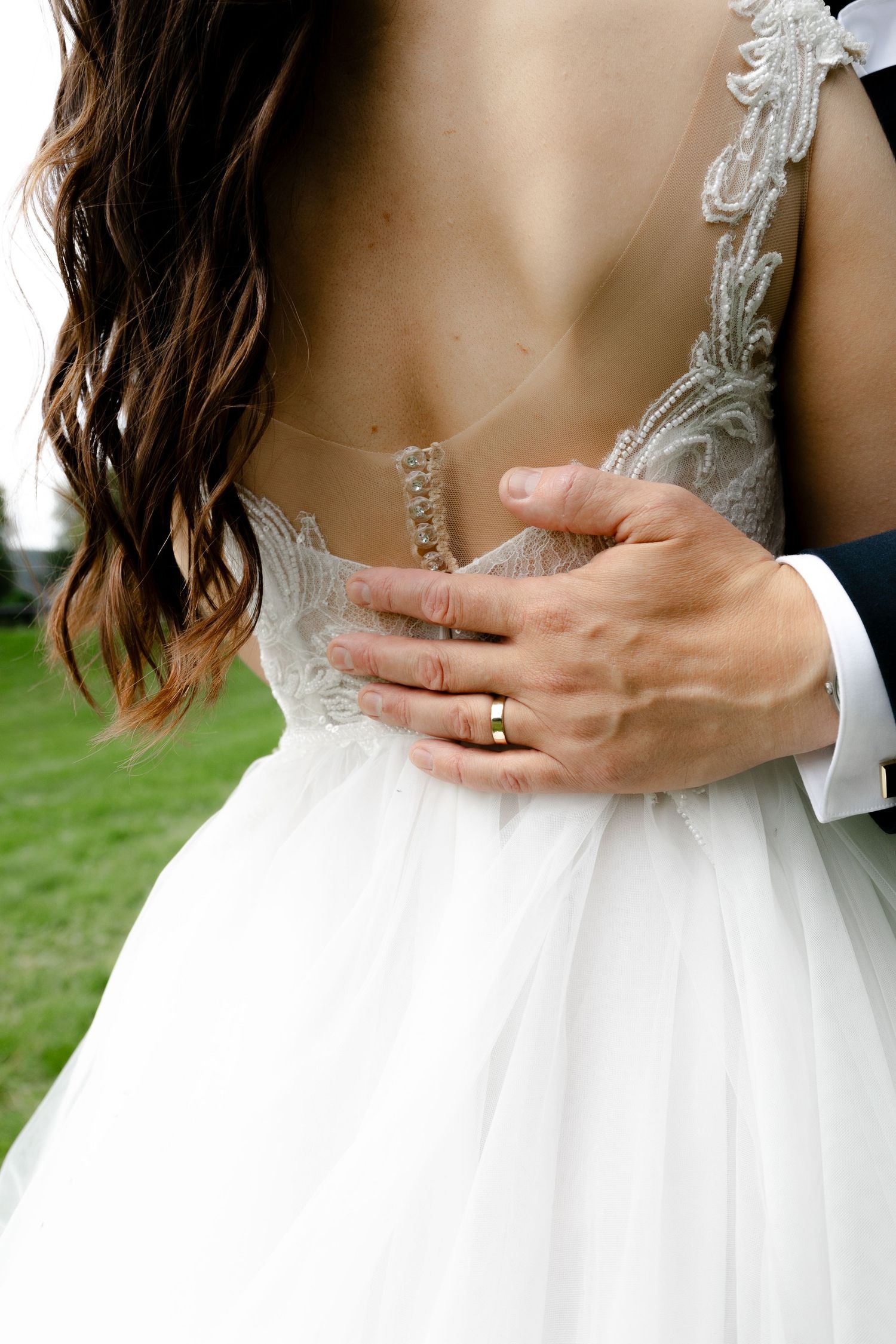 Close up of hands showing wedding ring details on bride's white lace dress.