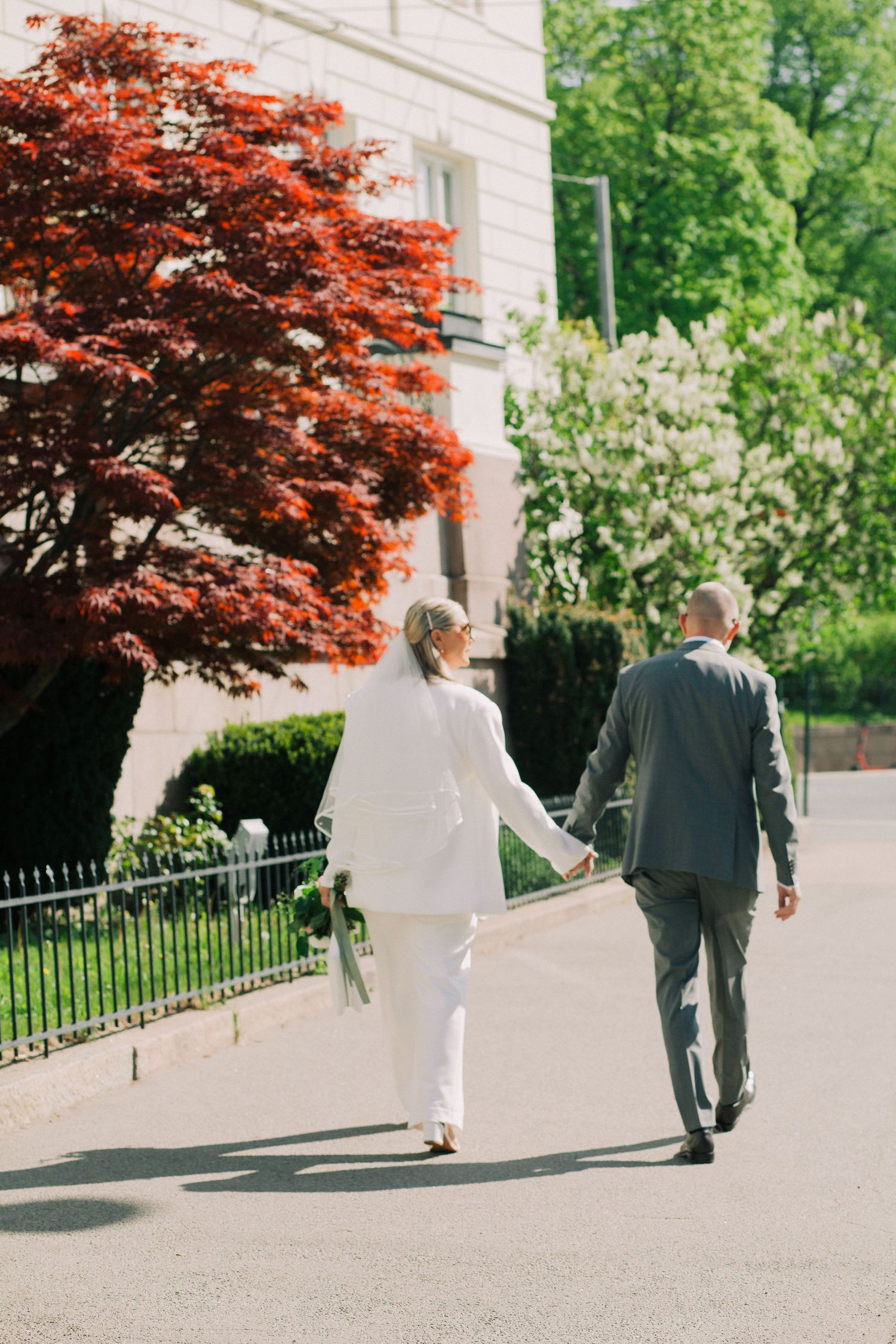 Two people walk along a path with vibrant red maple trees and green foliage in the background.