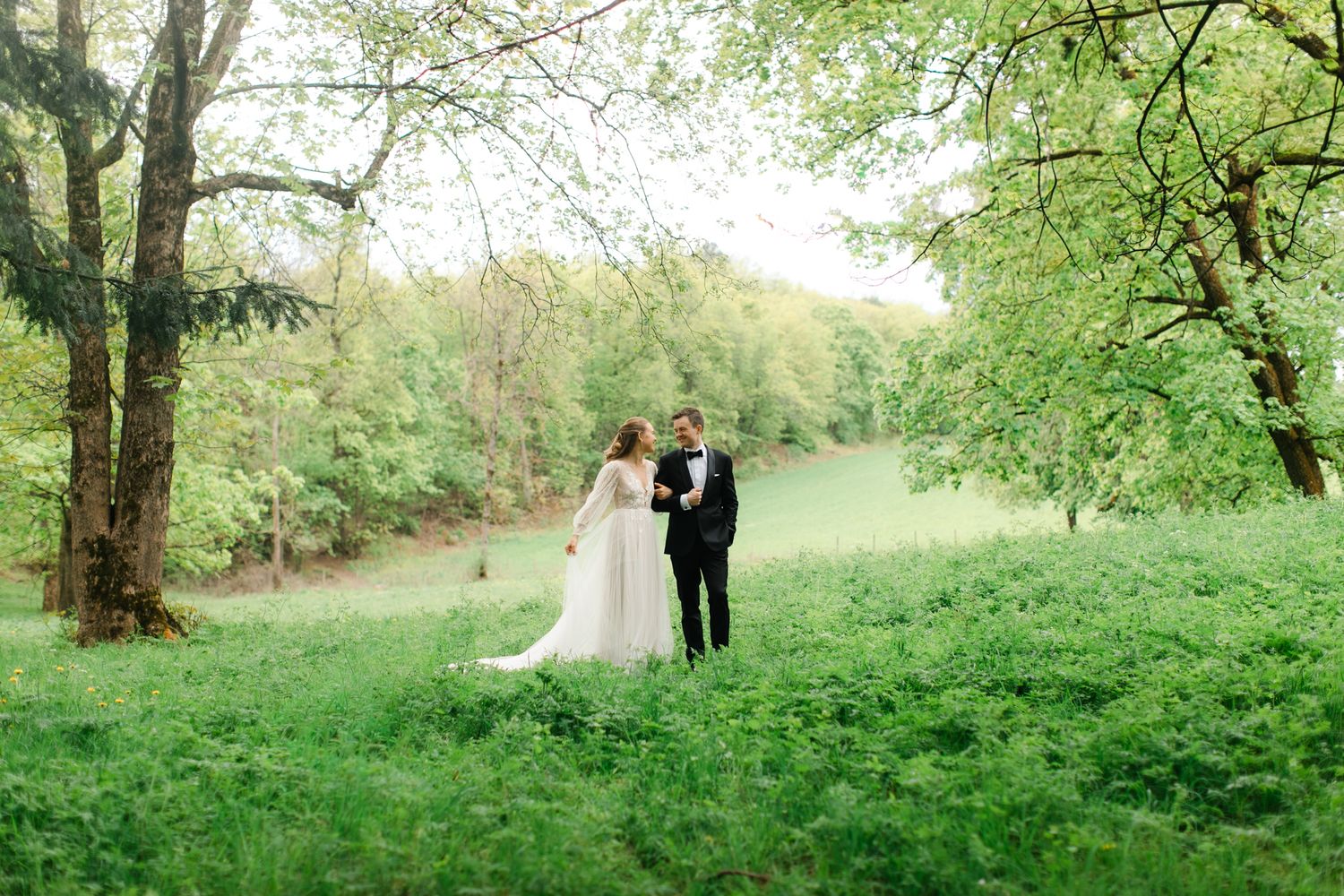 Bride and groom standing together in a lush green forest clearing, surrounded by tall trees on their wedding day.