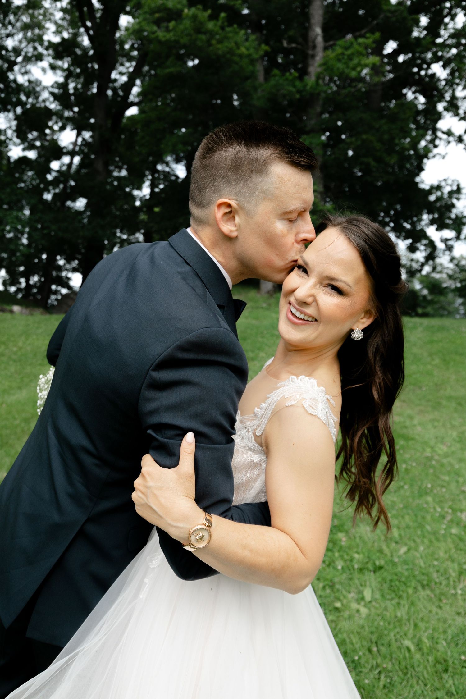 Newlywed couple shares romantic dance pose on grassy hillside during wedding photoshoot.