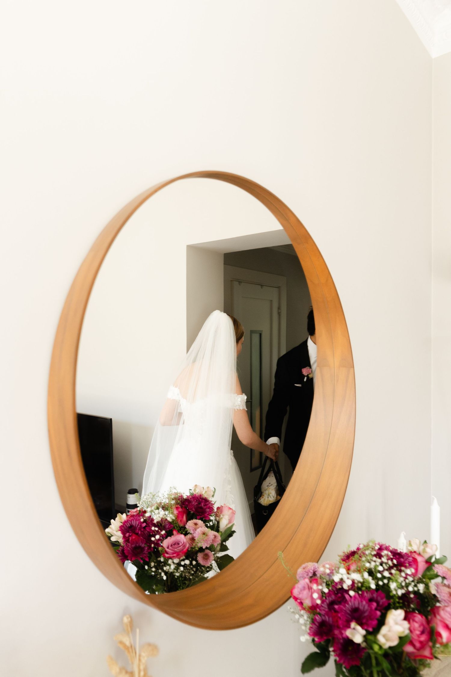 Three circular wooden mirrors mounted on white wall with pink and white floral arrangements below.