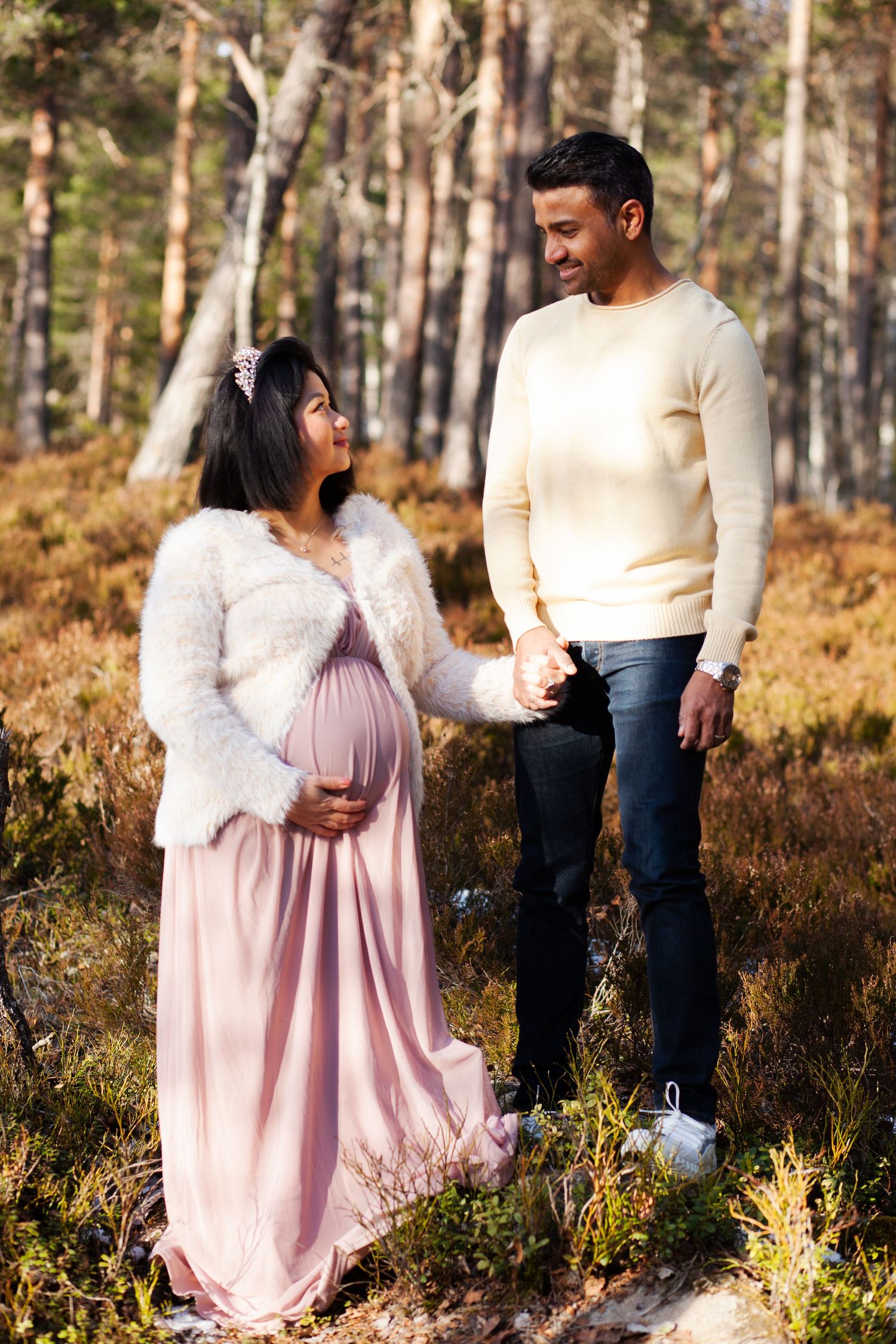 Outdoor maternity photoshoot with couple in forest setting during golden hour.