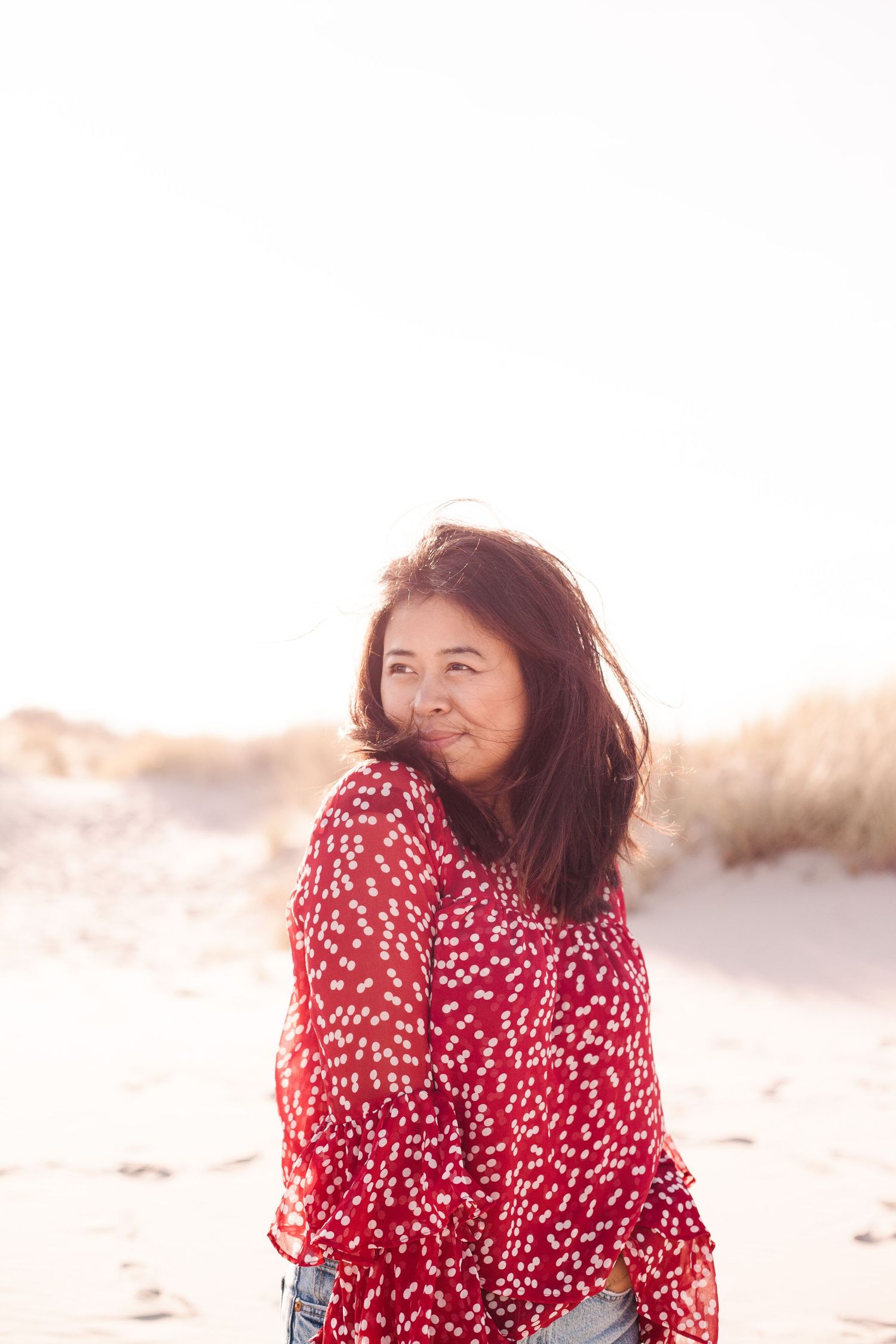 Woman in red and white polka dot dress twirls on beach at sunset creating dreamy romantic atmosphere.