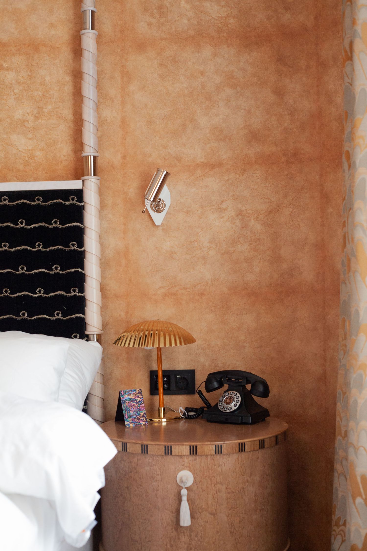 Vintage-style bedside table with rotary phone, table lamp, and white bedding.