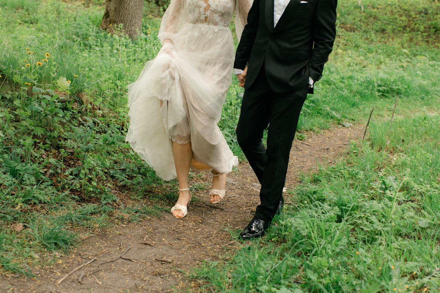 Bride and groom walking hand in hand on a garden path, bride in flowing gown, groom in black tuxedo.