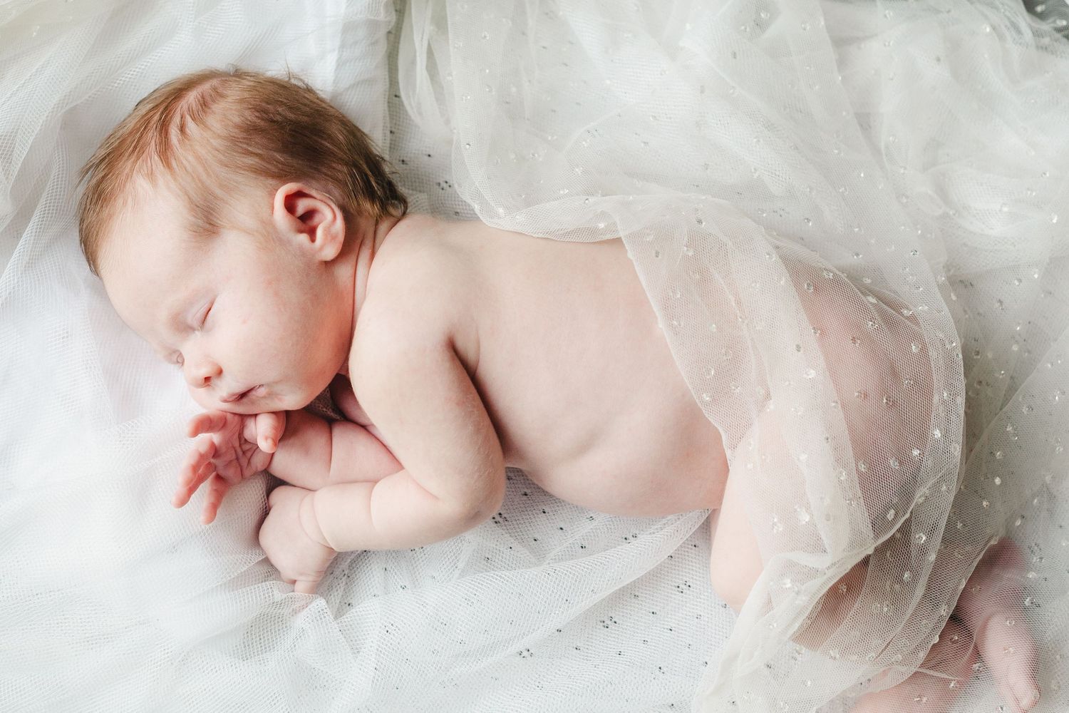 Sleeping infant wrapped in delicate white tulle fabric.