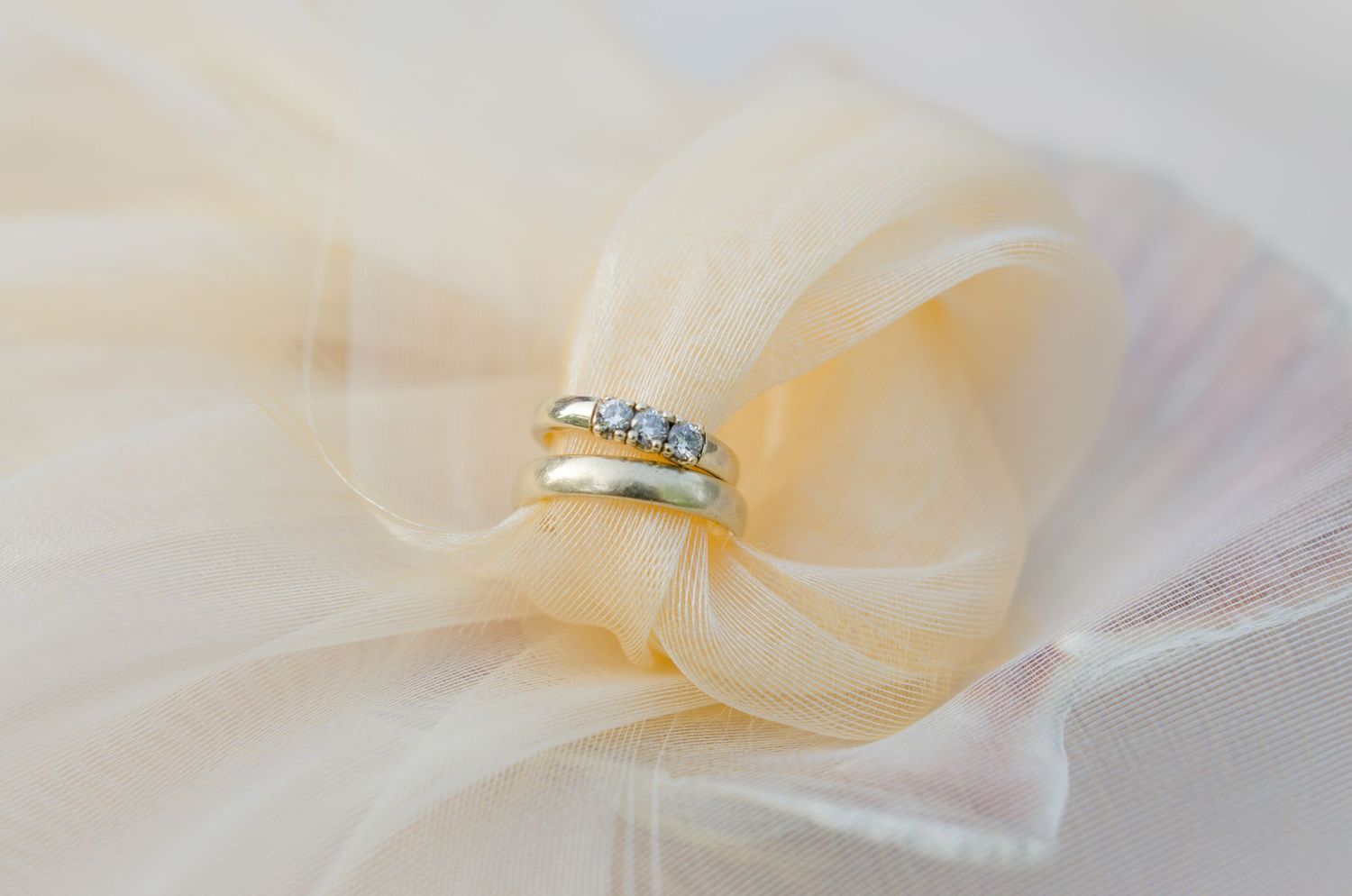 Elegant wedding rings on flowing sheer fabric in soft natural light.