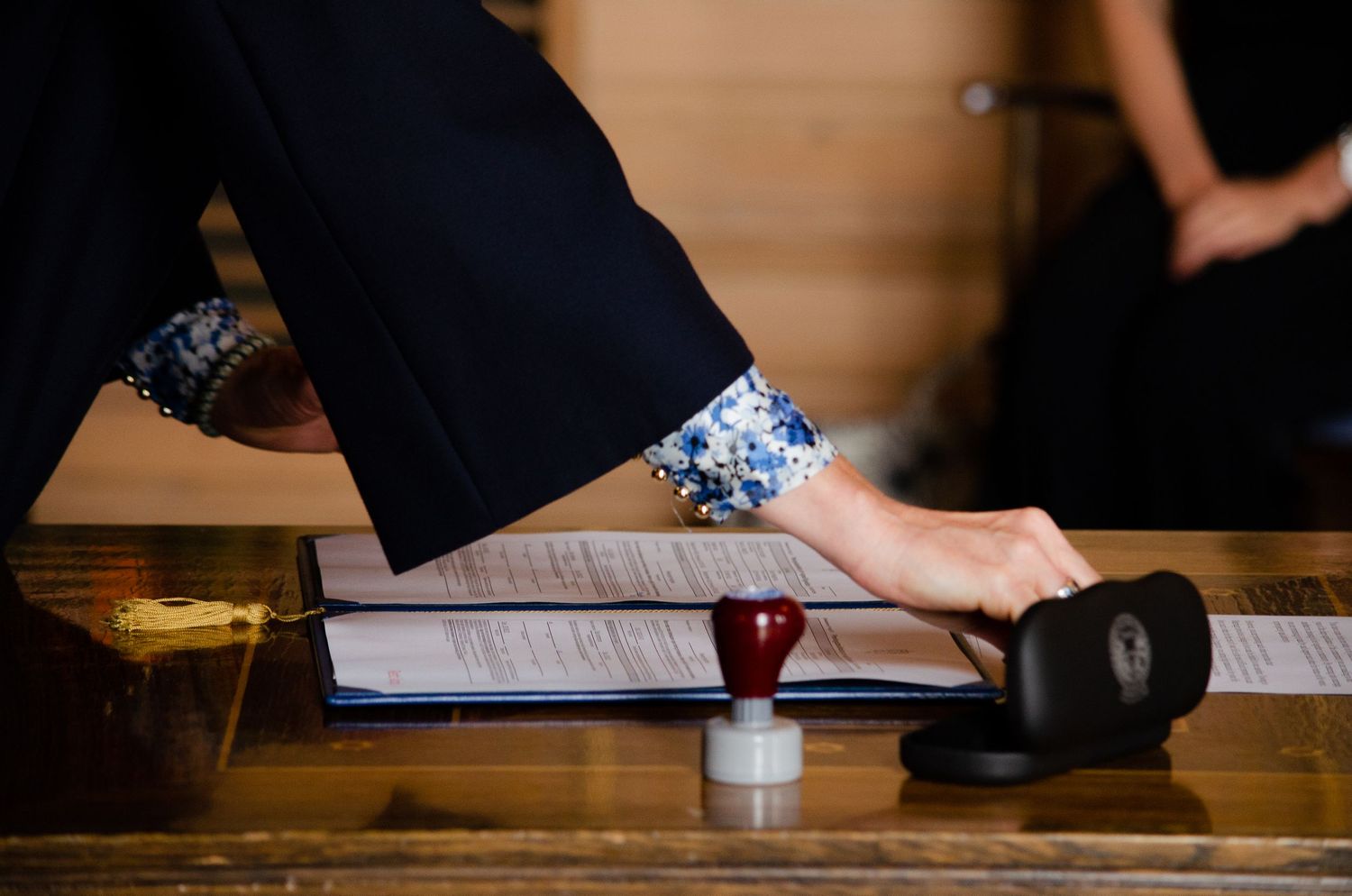 Hands signing official documents on a wooden table.