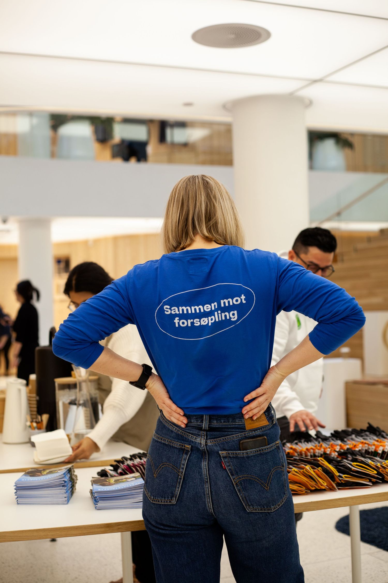 People in blue shirts and jeans examine merchandise displayed on tables at an indoor retail location.