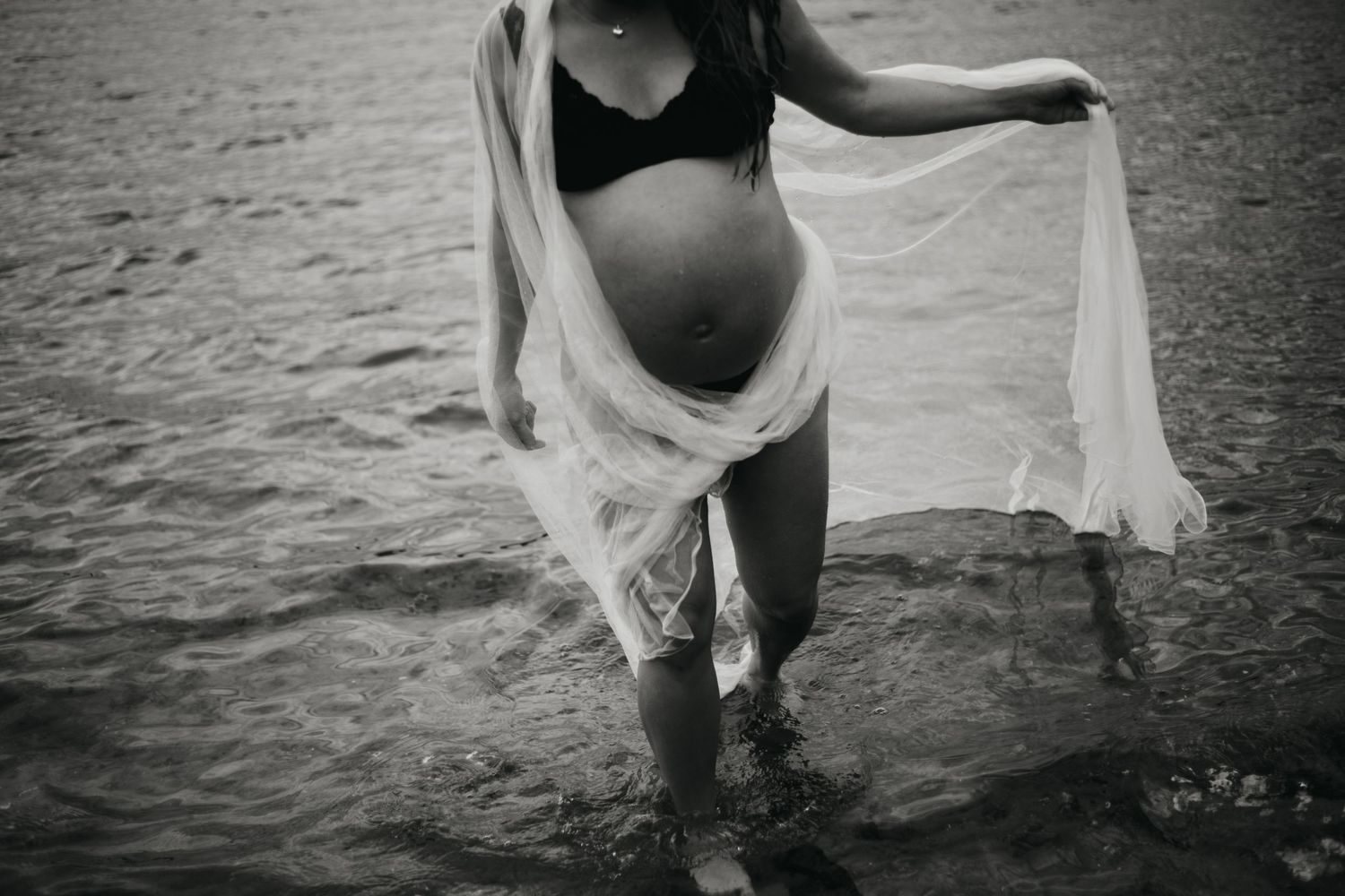 Maternity water photography session with flowing white dress in dark water.
