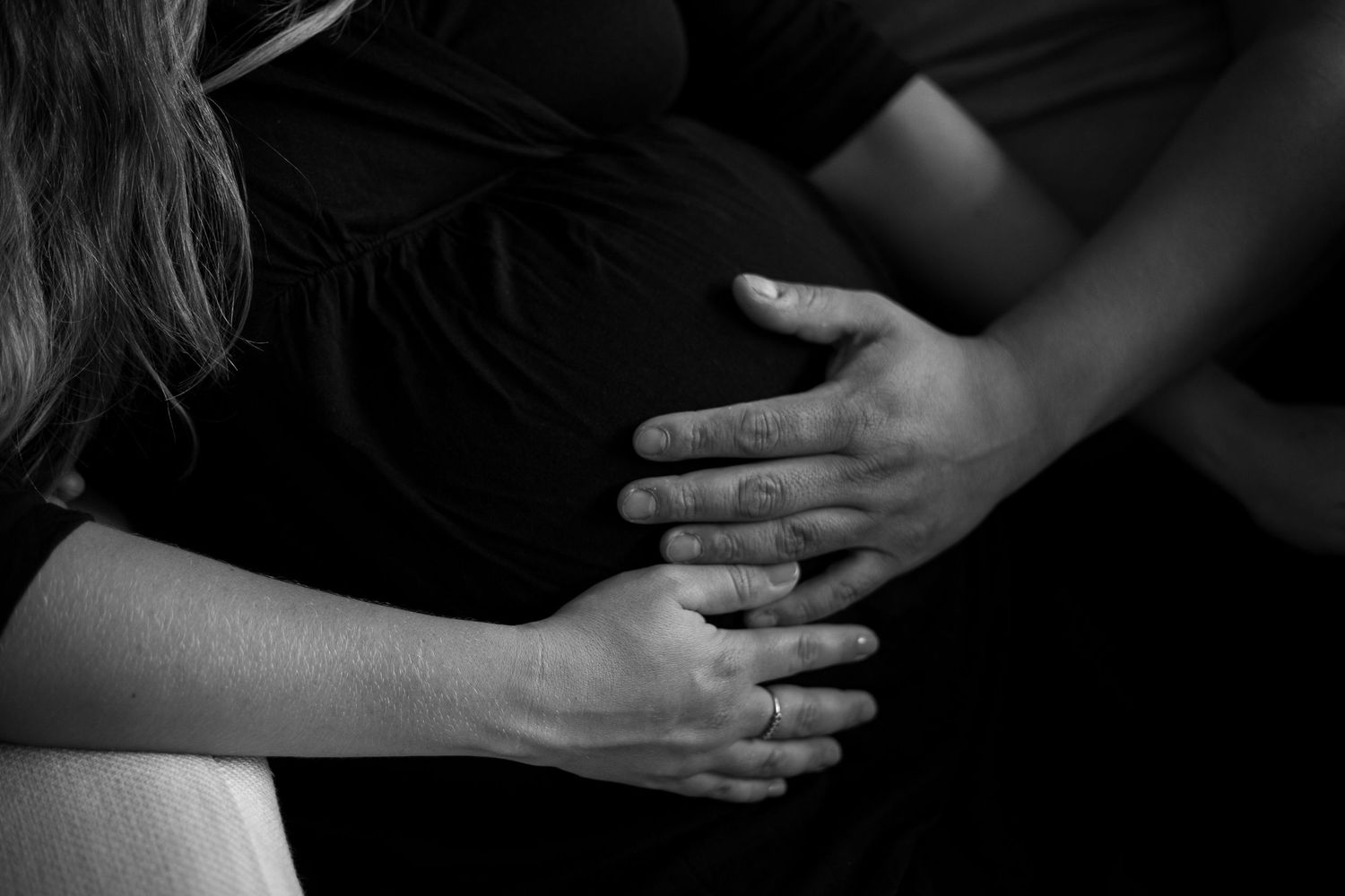 Black and white artistic close-up shots of hands cradling a pregnant belly.