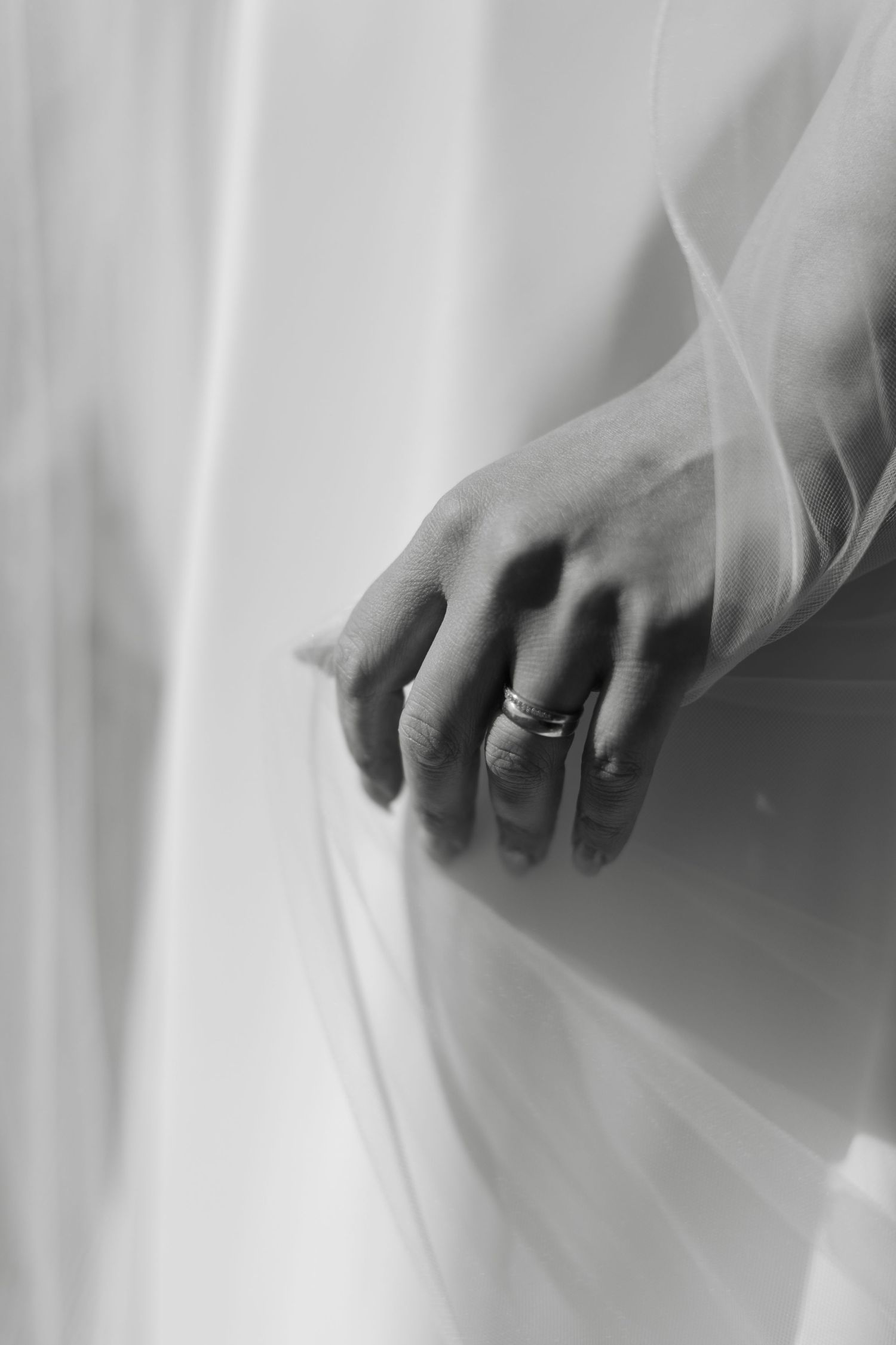 Close-up details of hands against flowing white wedding dress fabric.