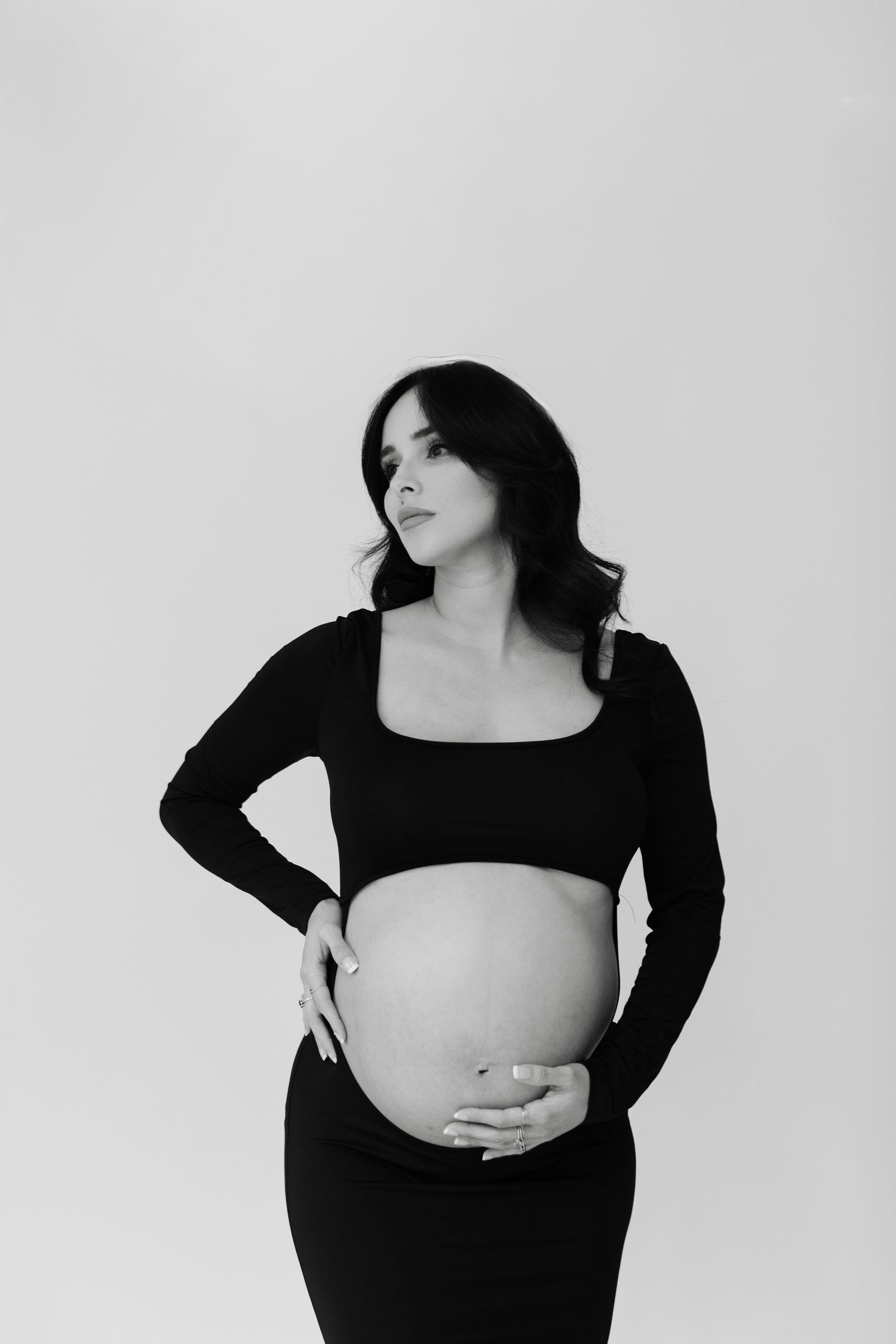 Artistic black and white maternity portrait against plain background.