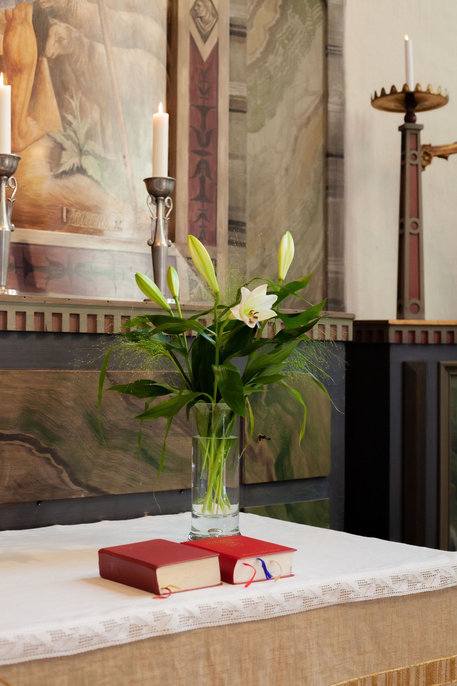 White lilies in a glass vase with a red book on a church altar.