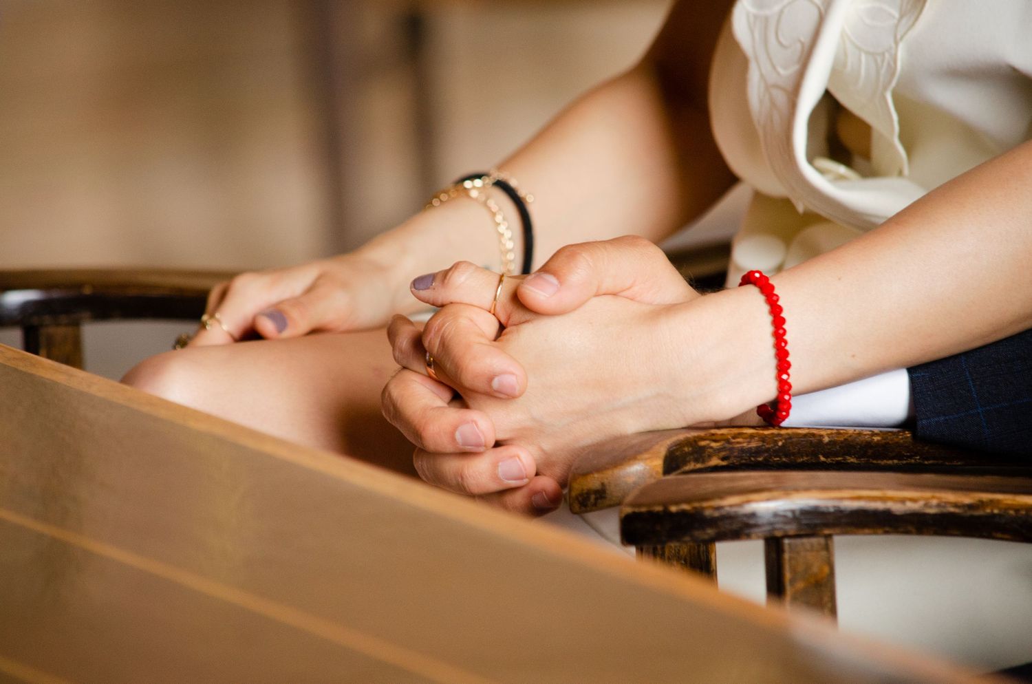 Close-up of hands resting on a wooden surface with a red bracelet detail.