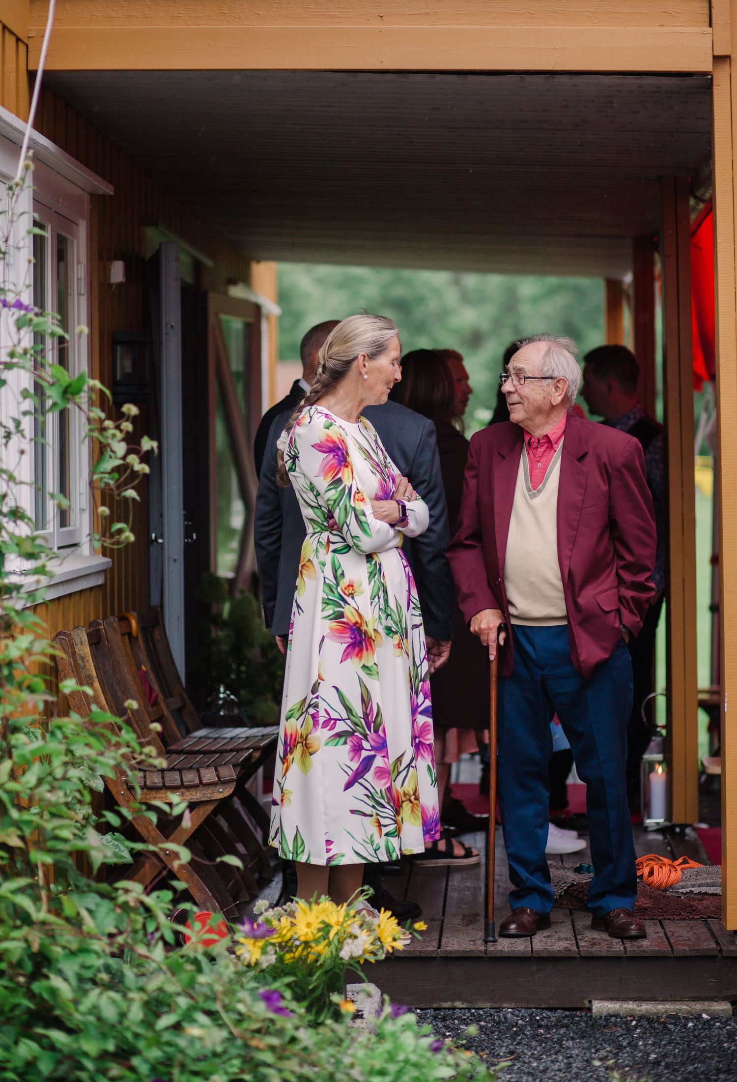 People gathering on a wooden porch decorated with flowers and greenery.