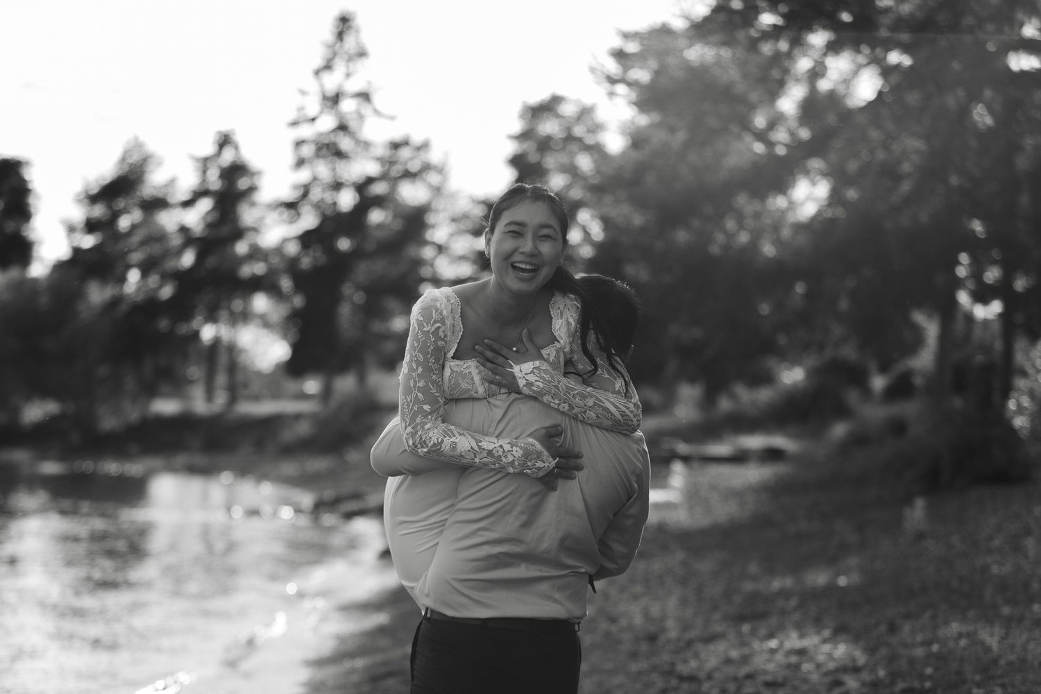 Black and white photo of a couple embracing outdoors in a natural setting.