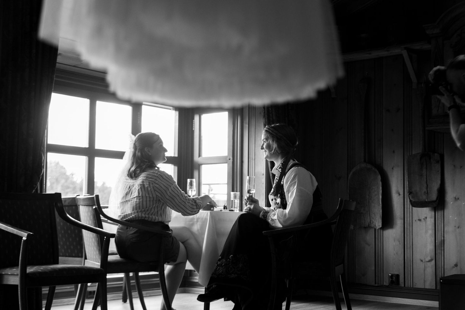 Two people sit in conversation by a window in a vintage black and white photograph.